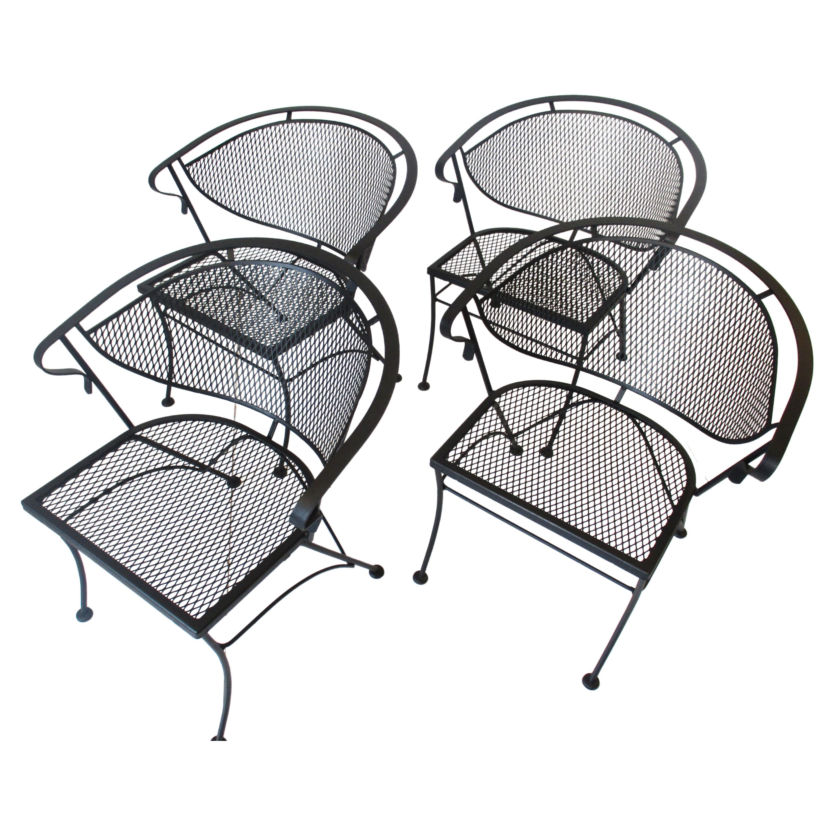 A set of four satin black mid century iron and steel mesh lounge chairs with wrap around backside and flat arm rail with nice stable foot pads. Manufactured by the Woodard furniture company known for their high quality construction and sharp style,
