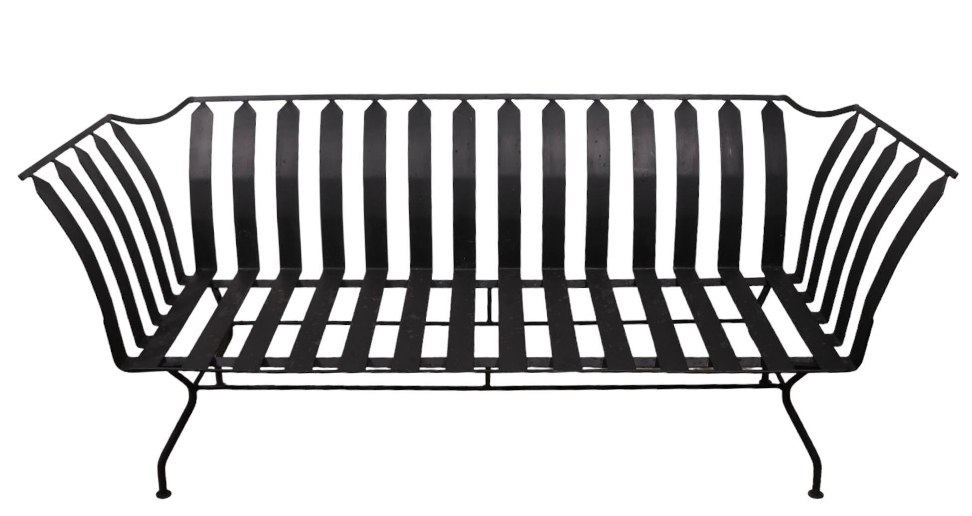 Chic Mid Century Gondola form  loveseat, sofa attributed to The Woodard Furniture Company. The sofa features a metal frame constructed of wrought iron with repeating metal straps, with original vinyl cushions. This example is in very good, clean
