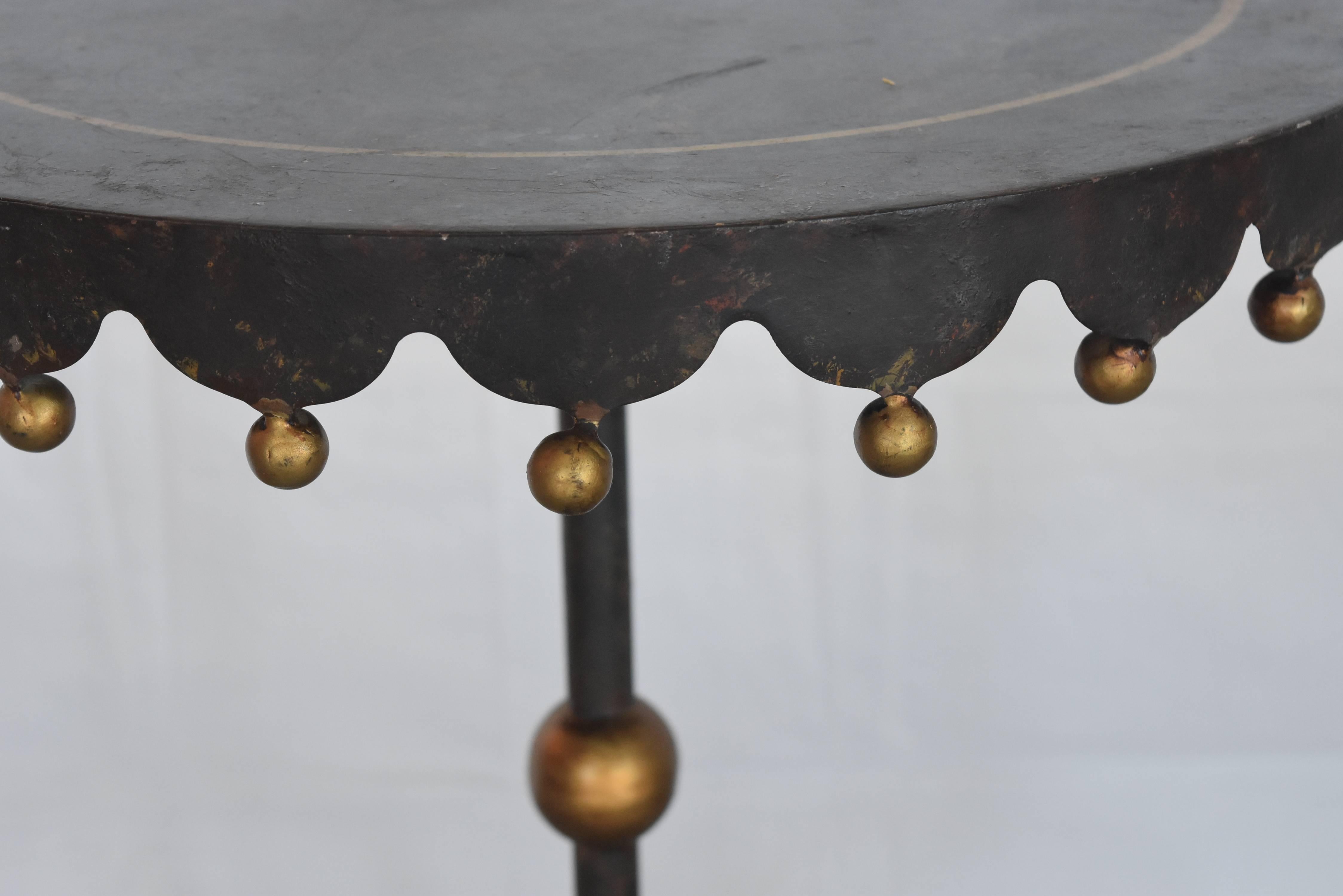 This little table originates from Spain, circa 1960s. It's got a heavy iron base with delicate gilt balls that dangle in place all around the skirt of the top as well as gold pin stripe all around the top perimeter. It's perfect for that small space