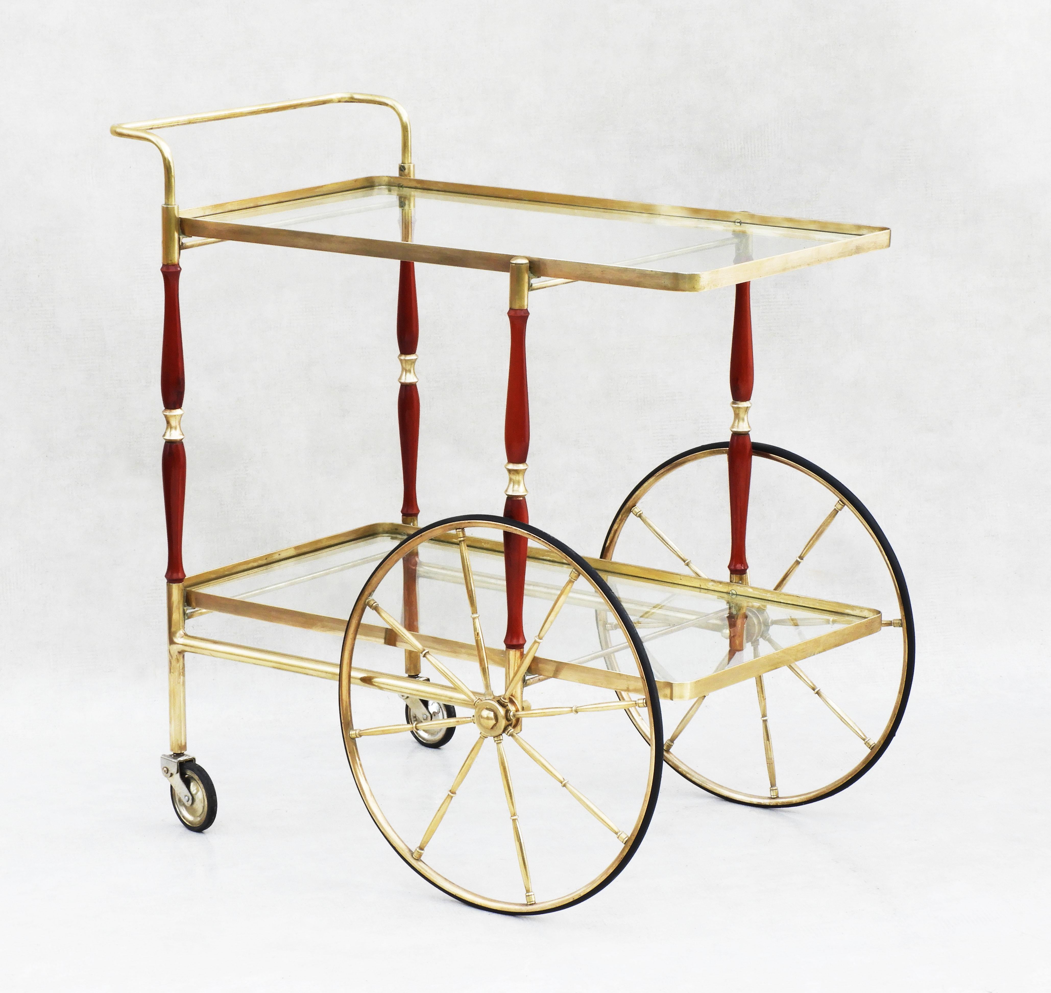 Vintage Mid Century Bar Cart c1950s Italy.  A stylish and practical, two-tiered, drinks trolley, bar cart or cocktail table with a brass frame and glass shelving, red wood detailing and oversized brass spoked wheels.  A nicely proportioned rolling