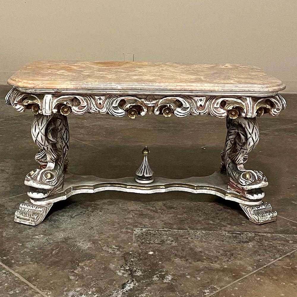 Mid-century Italian Baroque painted coffee table with travertine features a whimsical carving of a fish on each leg, all connected to an elaborate plateau fitted with extended feet and centered with a spire finial. The apron is an exaggerated