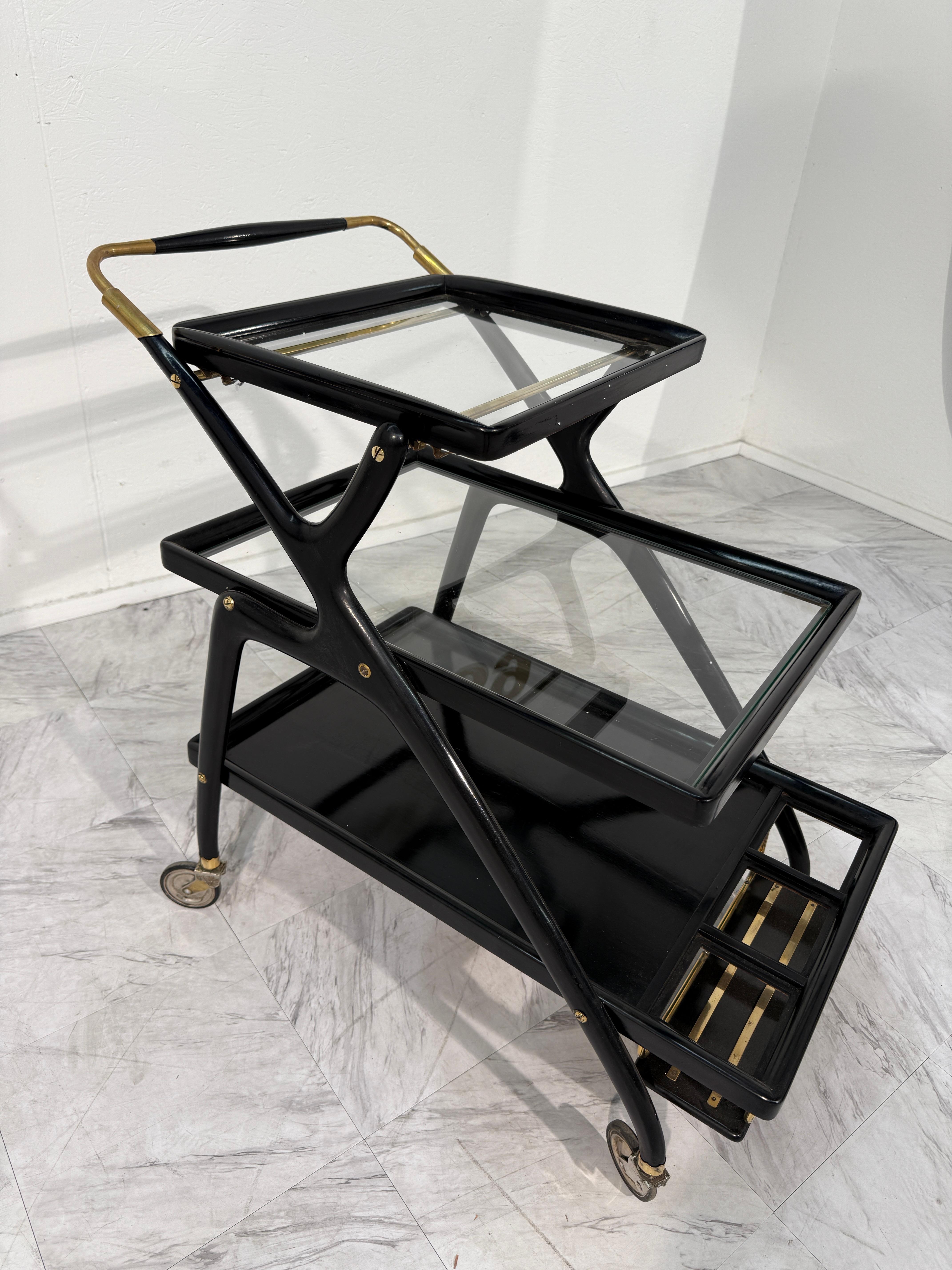 Elegante carrello da bar italiano di metà secolo con un'elegante struttura laccata nera con dettagli e accessori in ottone. Il carrello è progettato con due vassoi in vetro rimovibili che offrono stile e funzionalità, mentre il piano inferiore