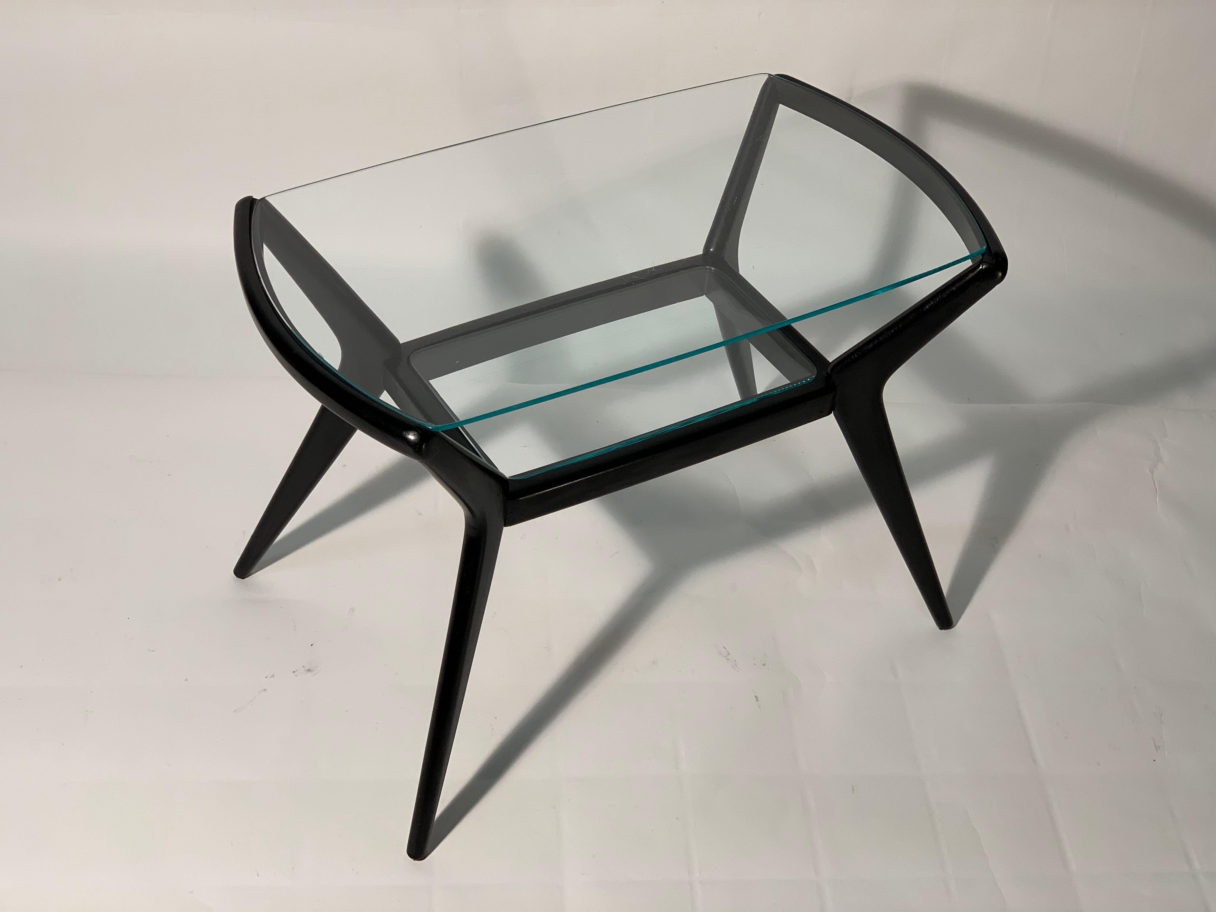 Italian midcentury 1950s double beveled glass shelves encased in a curved black lacquered wood structures.
The two shelves are supported by four elegant, strongly inclined, slender legs that taper towards the bottom.
This table can be used like
