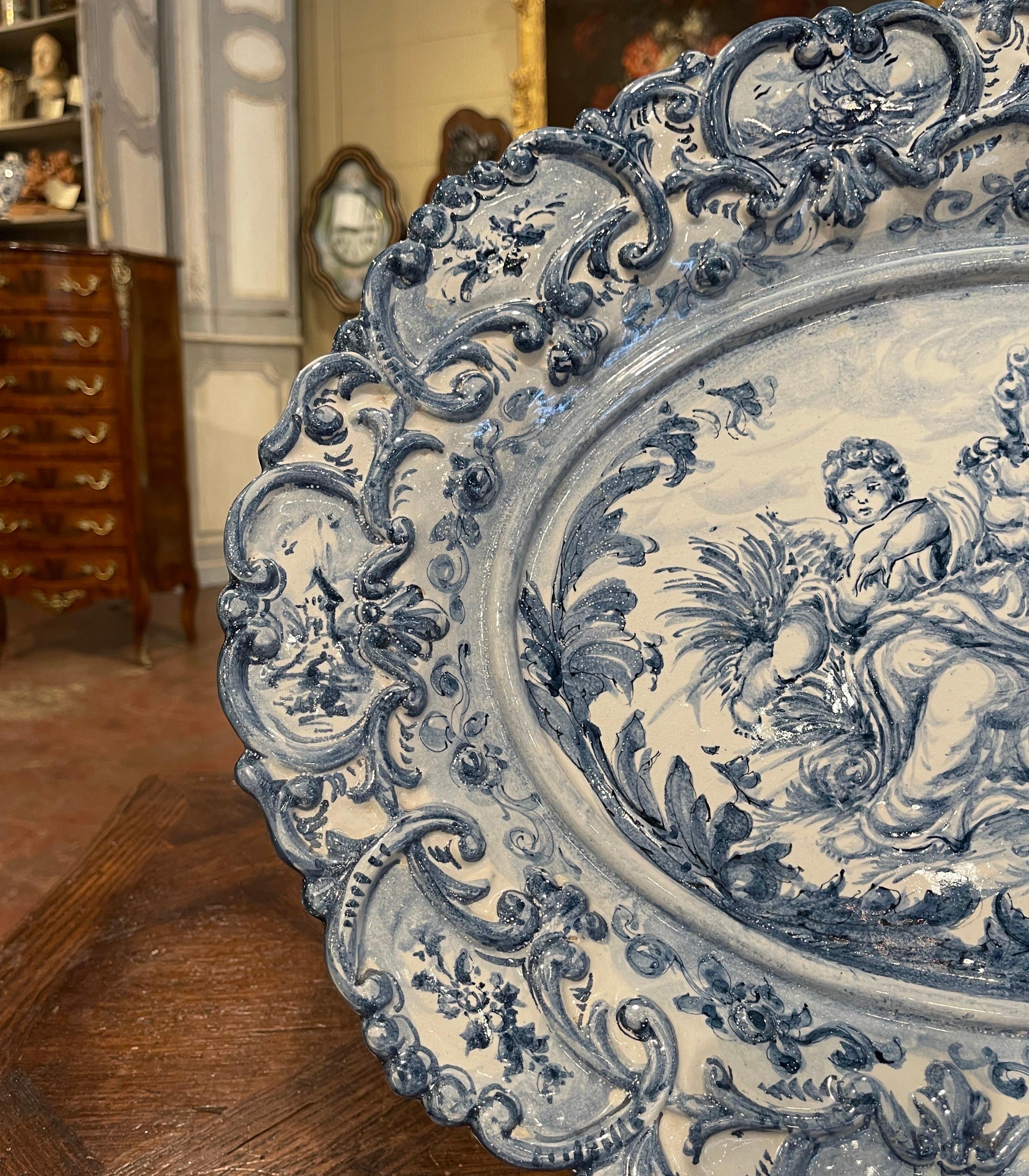 This large antique oval charger was crafted in Italy, circa 1960. The large ceramic wall hanging plate depicts a neoclassical outdoor scene with a young beauty and two cherubs at her side. The border in high relief is further embellished with floral