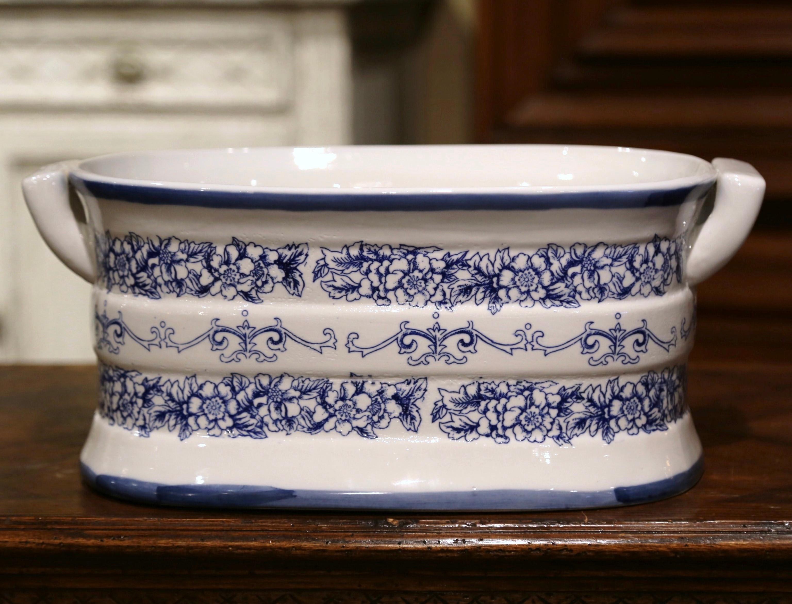 Crafted in Italy circa 1980 and oval in shape with bowed sides, the vintage porcelain basin is dressed with two side handles; it is decorated with hand painted floral motifs in the Delft blue and white palette. This elegant and colorful jardinière