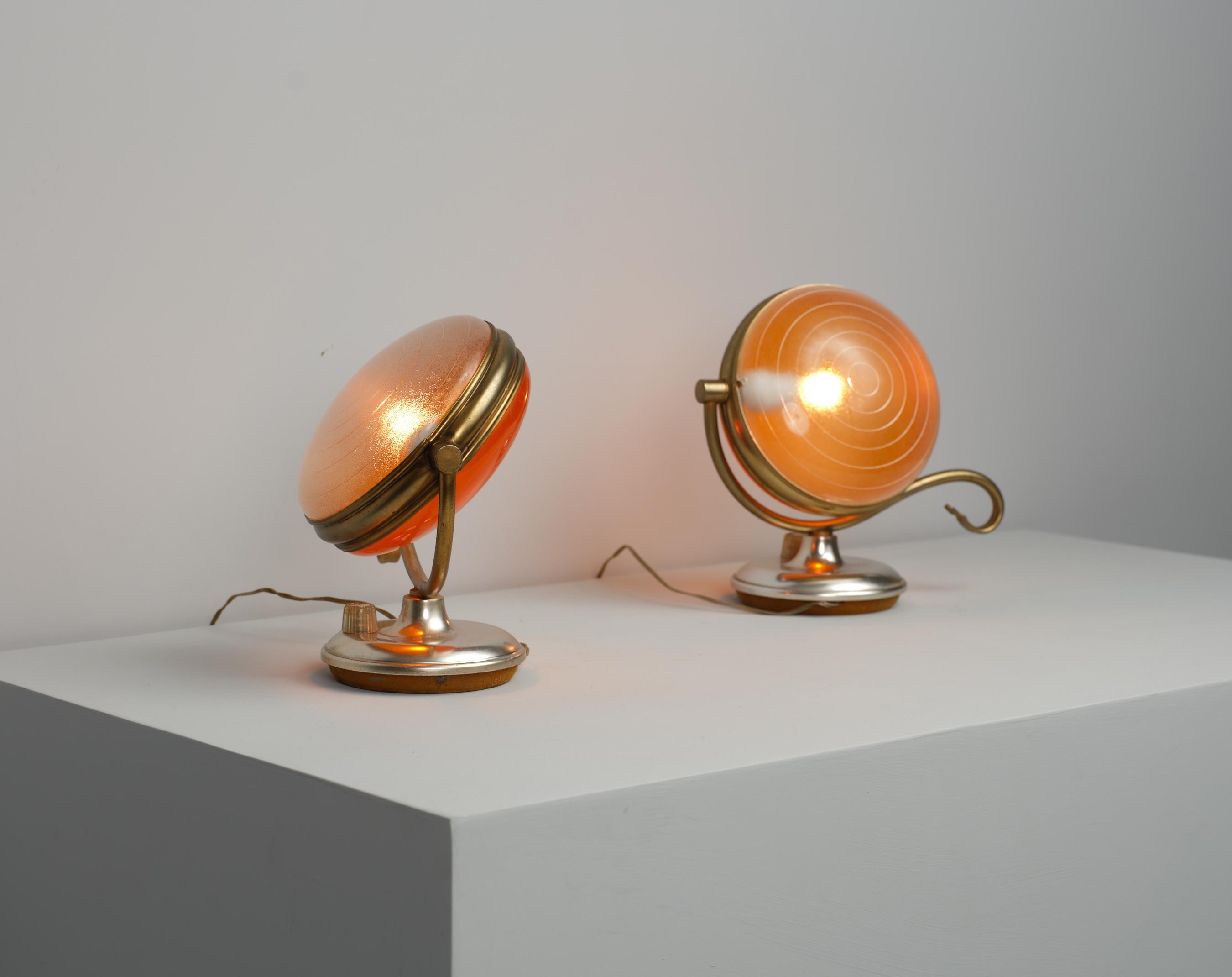 This set of two table lamps, originating from 1950s Italy, features a distinctive mid-century design with elements of brass and metal. The lamps boast a globe-like shape, enhancing their aesthetic and functional appeal. The dual-tone shades can be