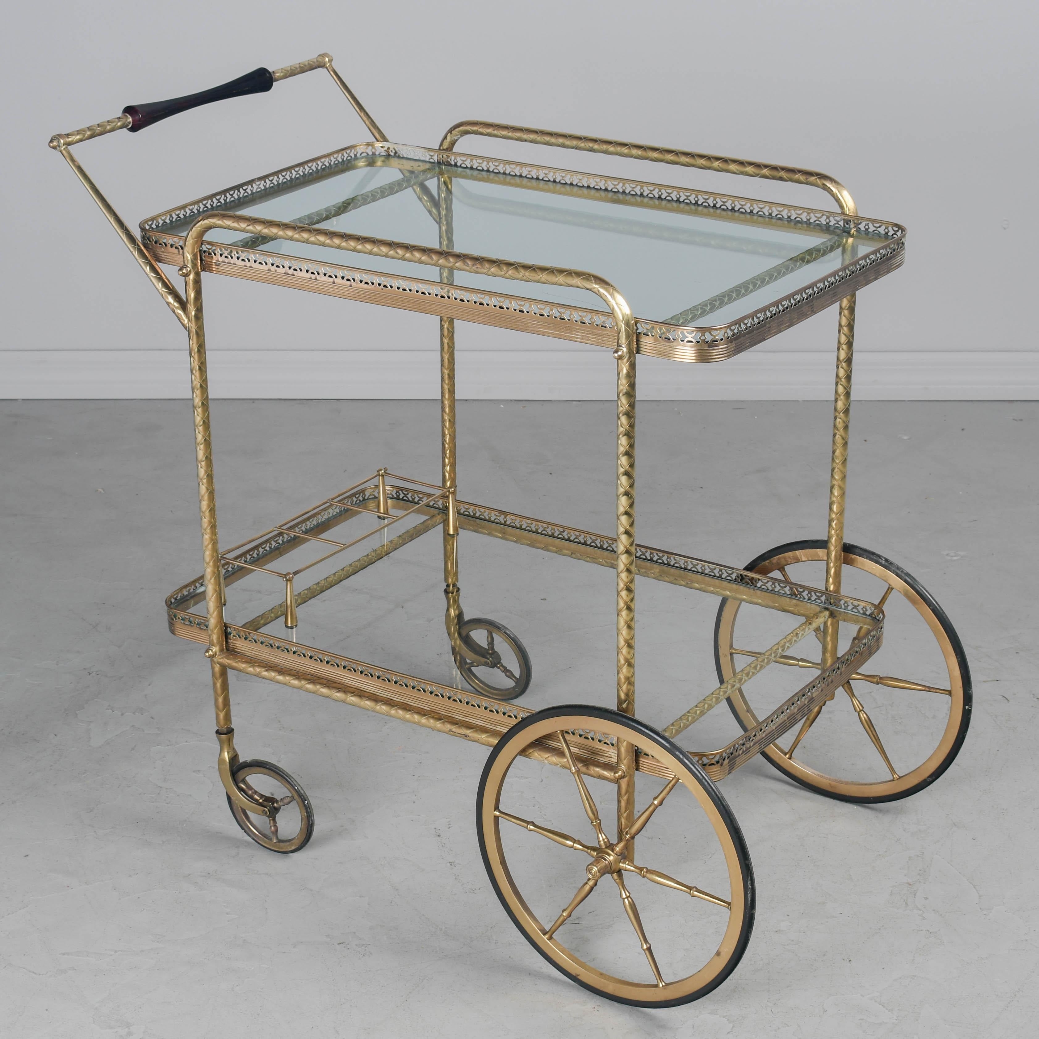 Carrito de bar italiano de latón moderno de mediados de siglo, con asa de caoba y estantes de cristal con botellero. Conservando un bonito aspecto de pulido brillante. Rueda suavemente. Circa 1950s. 34,5