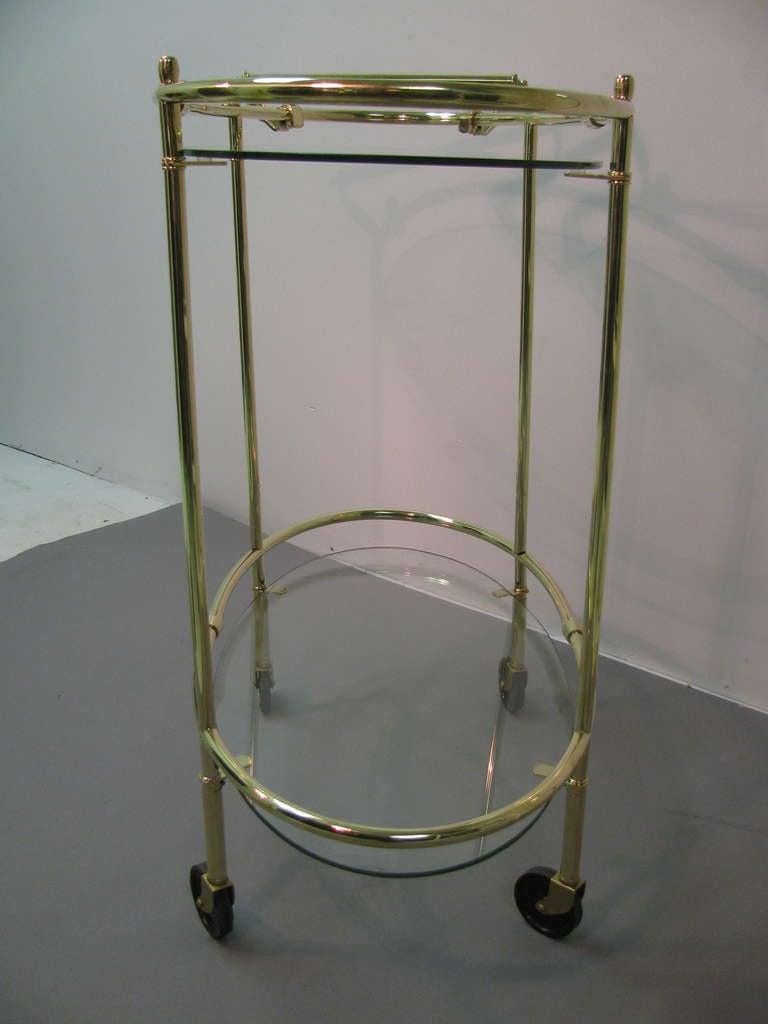 Beautiful and recently polished oval brass bar cart in a simplistic and elegant form. Original glass panels. 34in. To top of handle. In excellent vintage condition with minimal wear. Glides freely