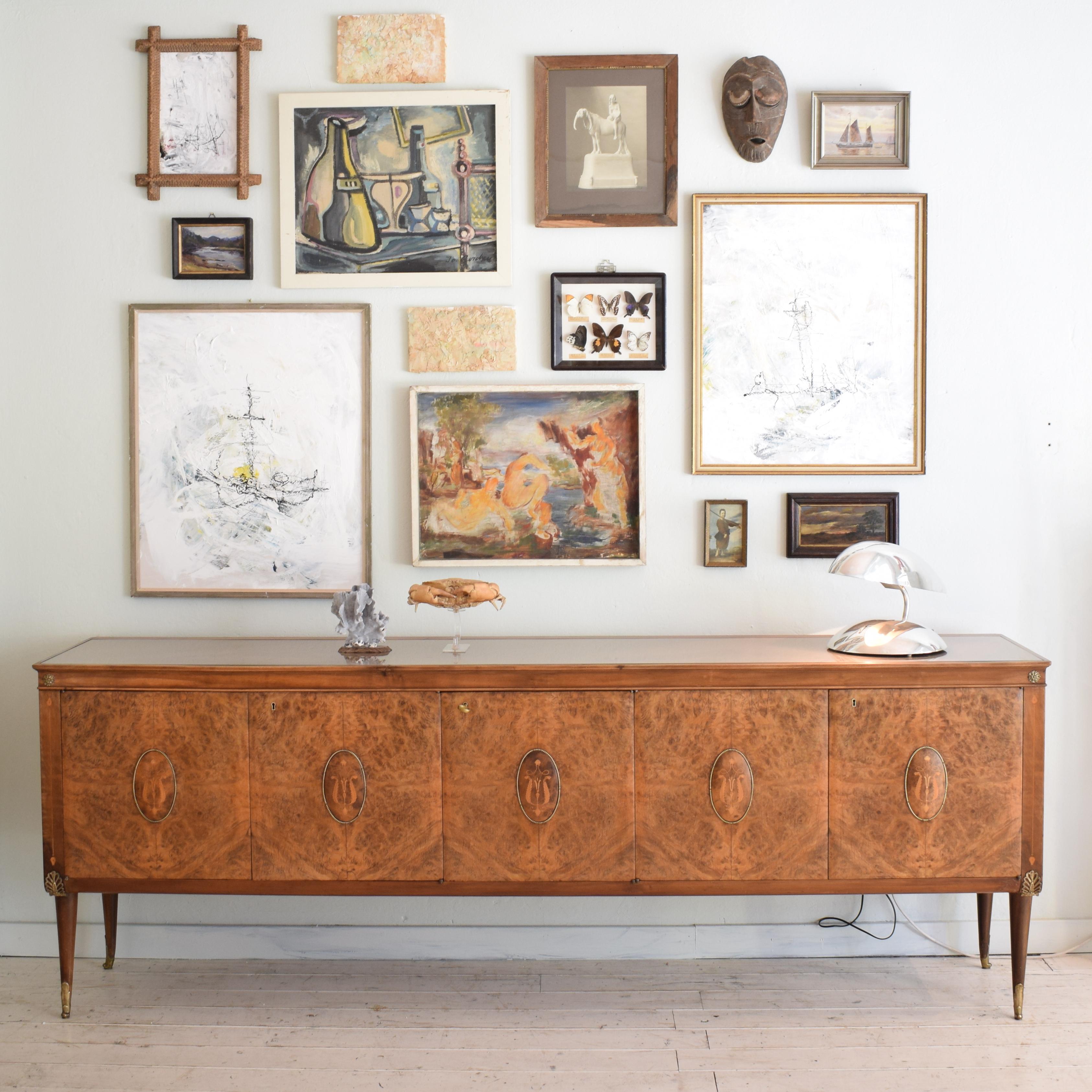 This elegant large midcentury Italian brown sideboard in the style of Paolo Buffa was made in the 1940s.
It is in walnut, burr walnut and has got some beautiful Marquetry details. Also the brass leg shoes are very special. The top of the sideboard