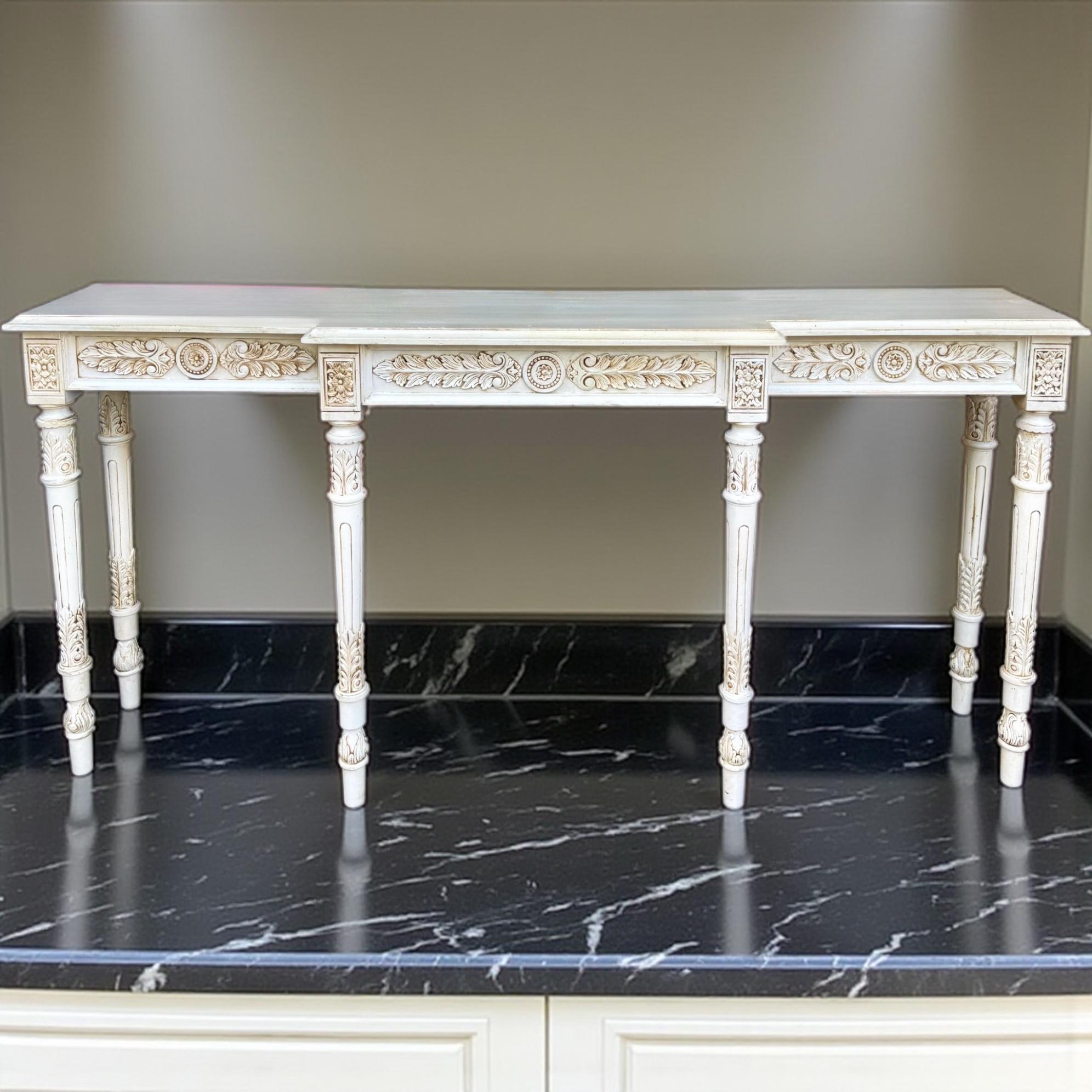 This is a mid-century Italian elongated carved and painted console table with French Louis XVI styling. It is white with a nicely carved apron and tapered fluted leges. Its nice slim size makes it a great size for a variety of spaces. It is unmarked