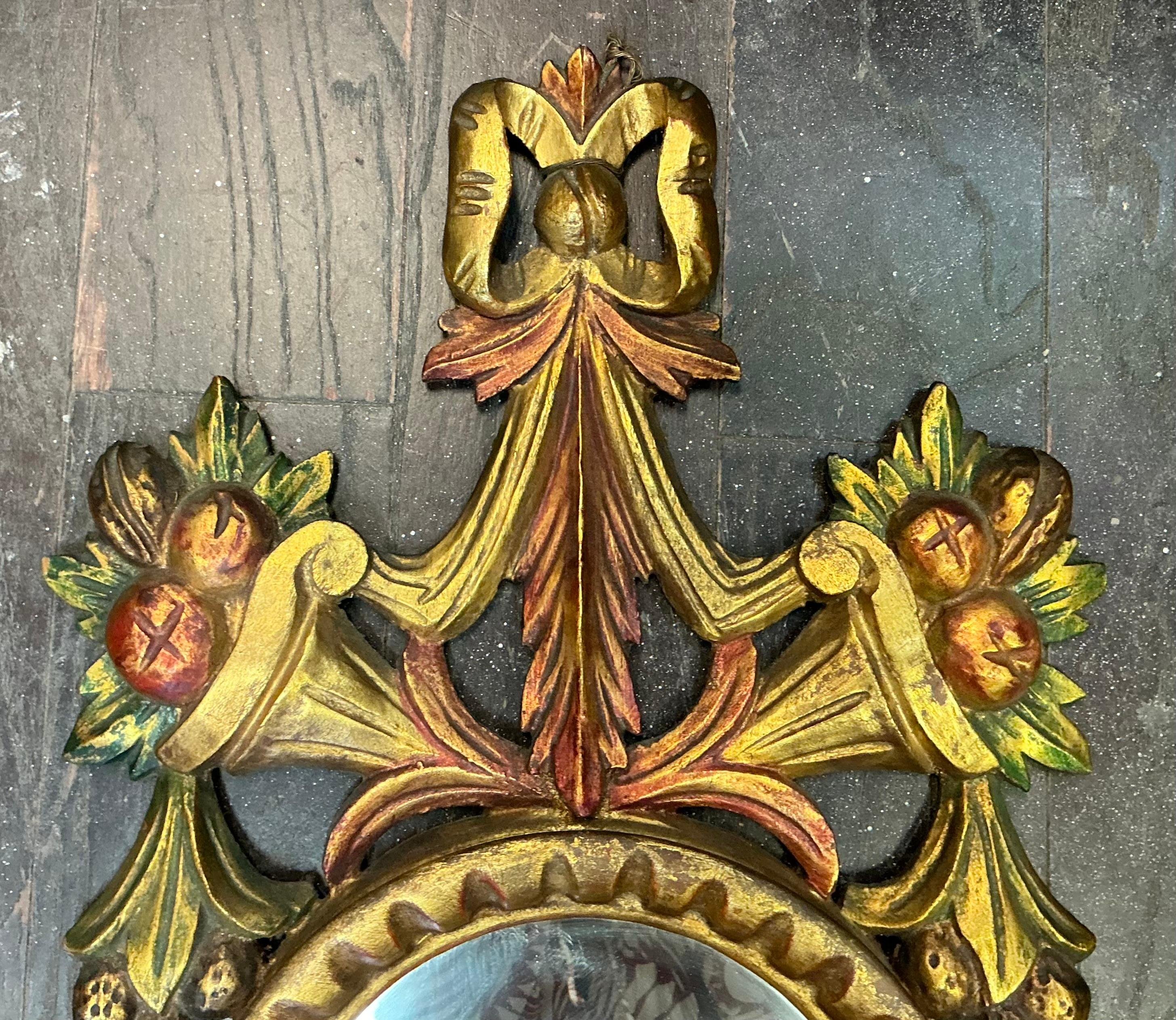 This is a mid-century carved giltwood Italian wall mirror. It has painted cornucopias with fruit and flowing ribbon detail. It is unmarked and in very good condition.