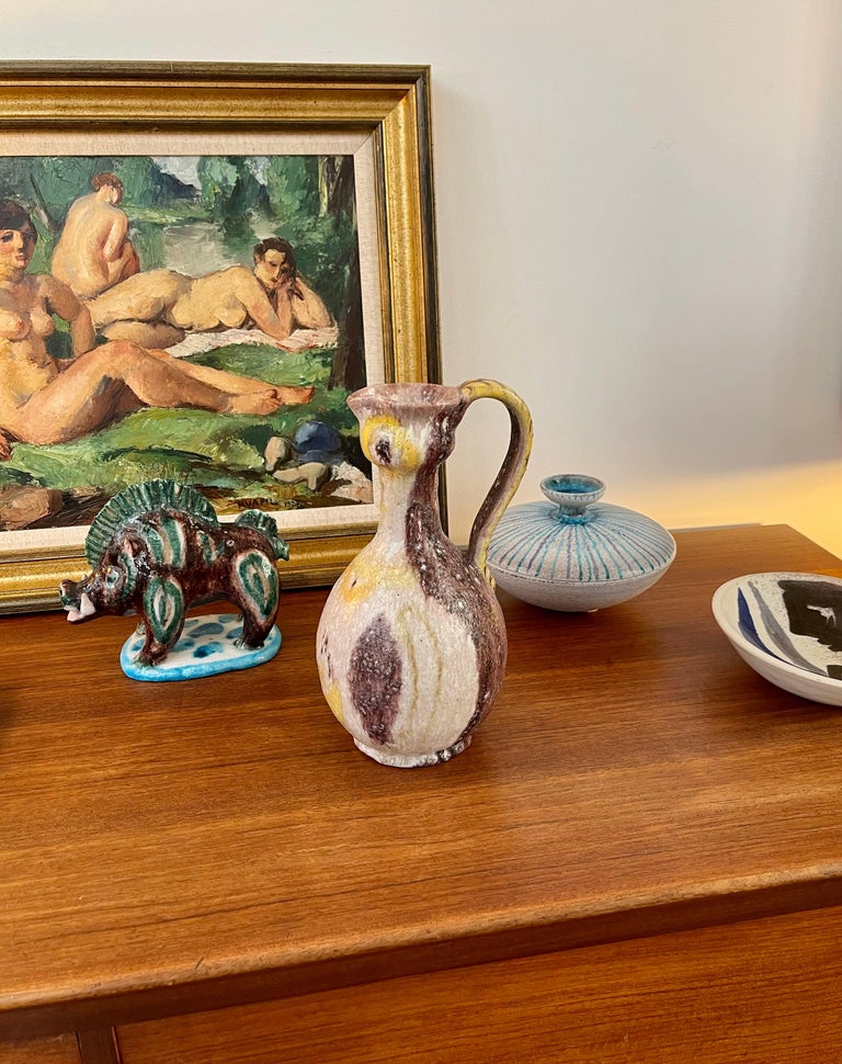 Midcentury Italian decorative ceramic pitcher by Guido Gambone (circa 1950s). The classically-shaped pitcher is reminiscent of earthenware from ancient Greece and Rome, particularly its large, arching handle. A lustrous glaze over the magenta,
