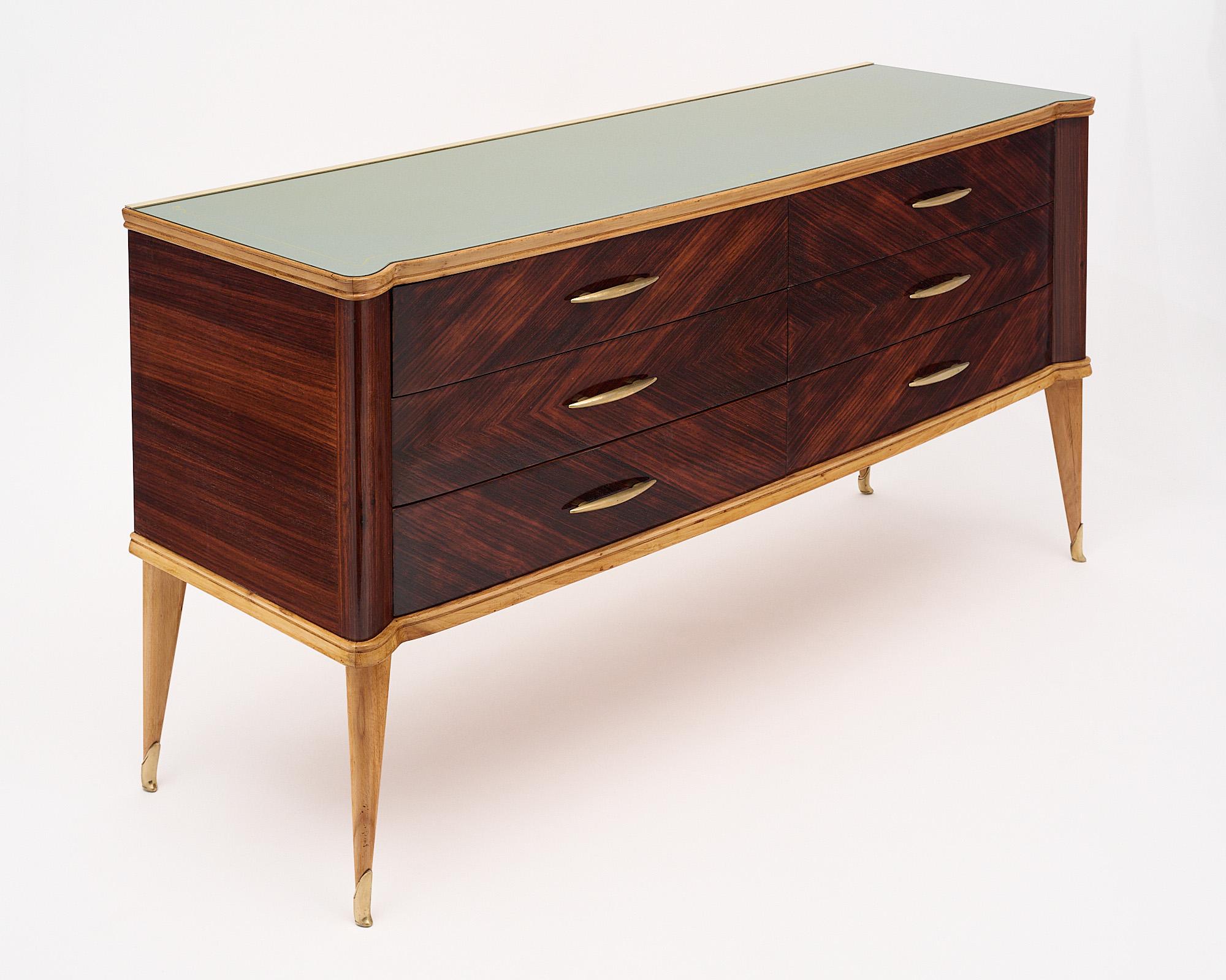 Chest of drawers from Italy with a beautiful rosewood veneer and glass top. There are six dovetailed drawers with brass hardware on each. A lighter wood frames the body of the chest and holds the frosted glass top in place. The four tapered legs are