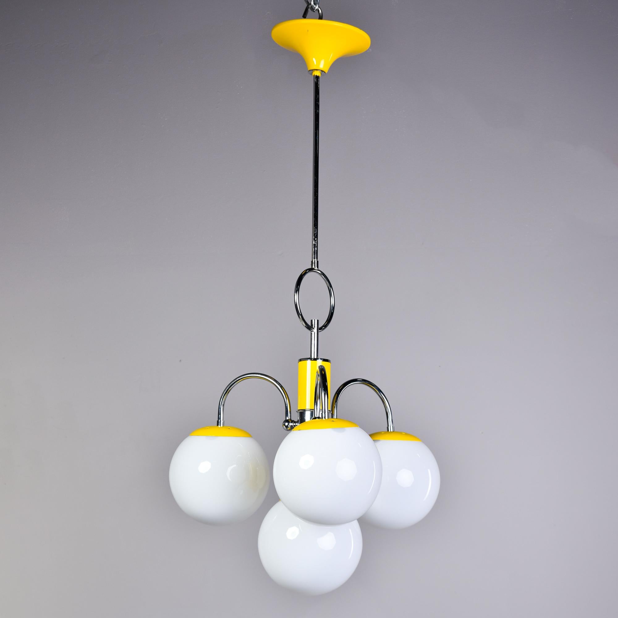 Found in Italy, this four light fixture dates from the early 1970s. Polished chrome frame with sunny yellow enamel accents and four white glass globes. Each globe has a single internal standard sized light socket. Wiring has been updated for US