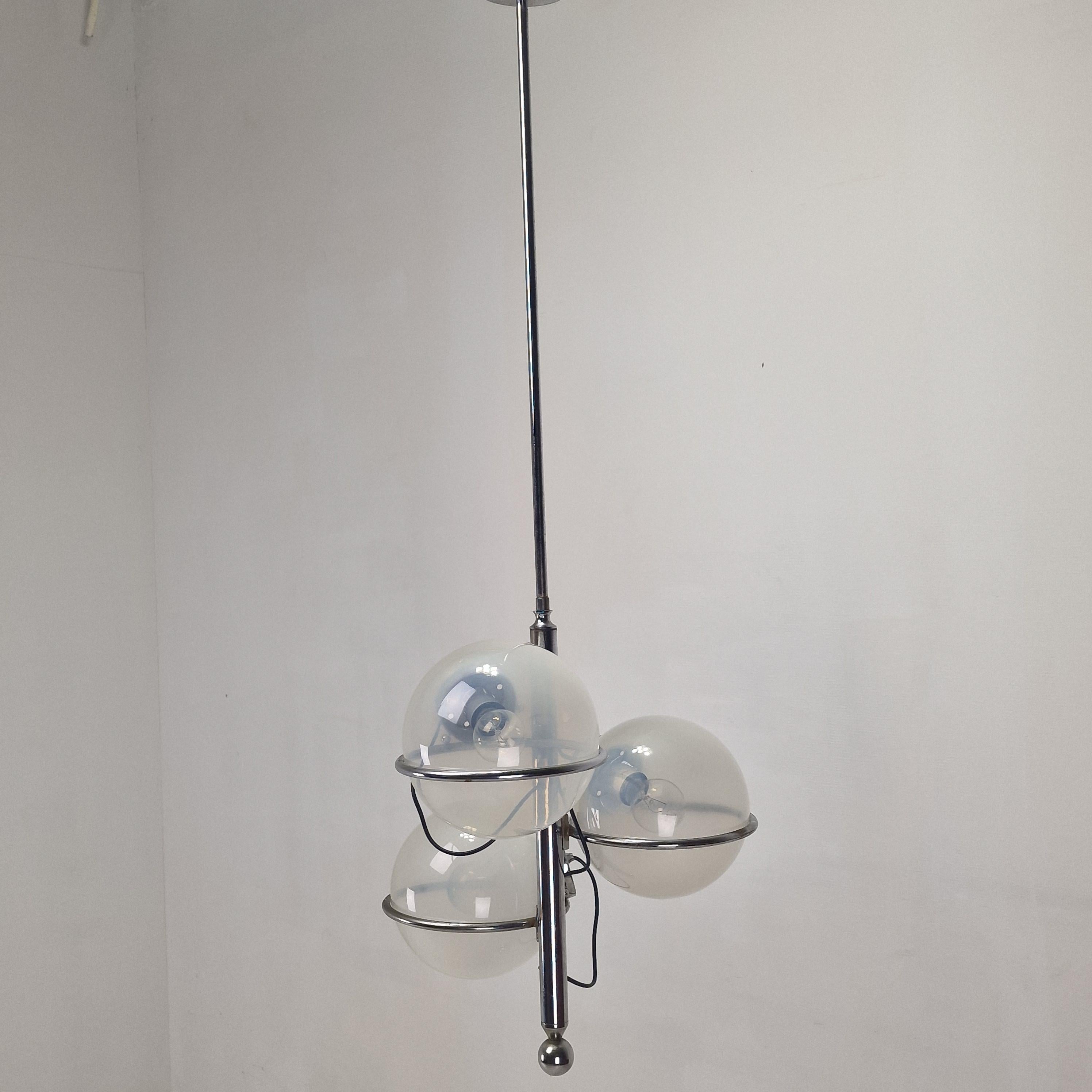 Sorprendente ejemplo del diseño italiano de los años 70, esta lámpara vintage presenta una elegante estructura cromada combinada con tres globos de cristal opalino que emiten un suave resplandor ambiental. 

El armonioso contraste entre el metal