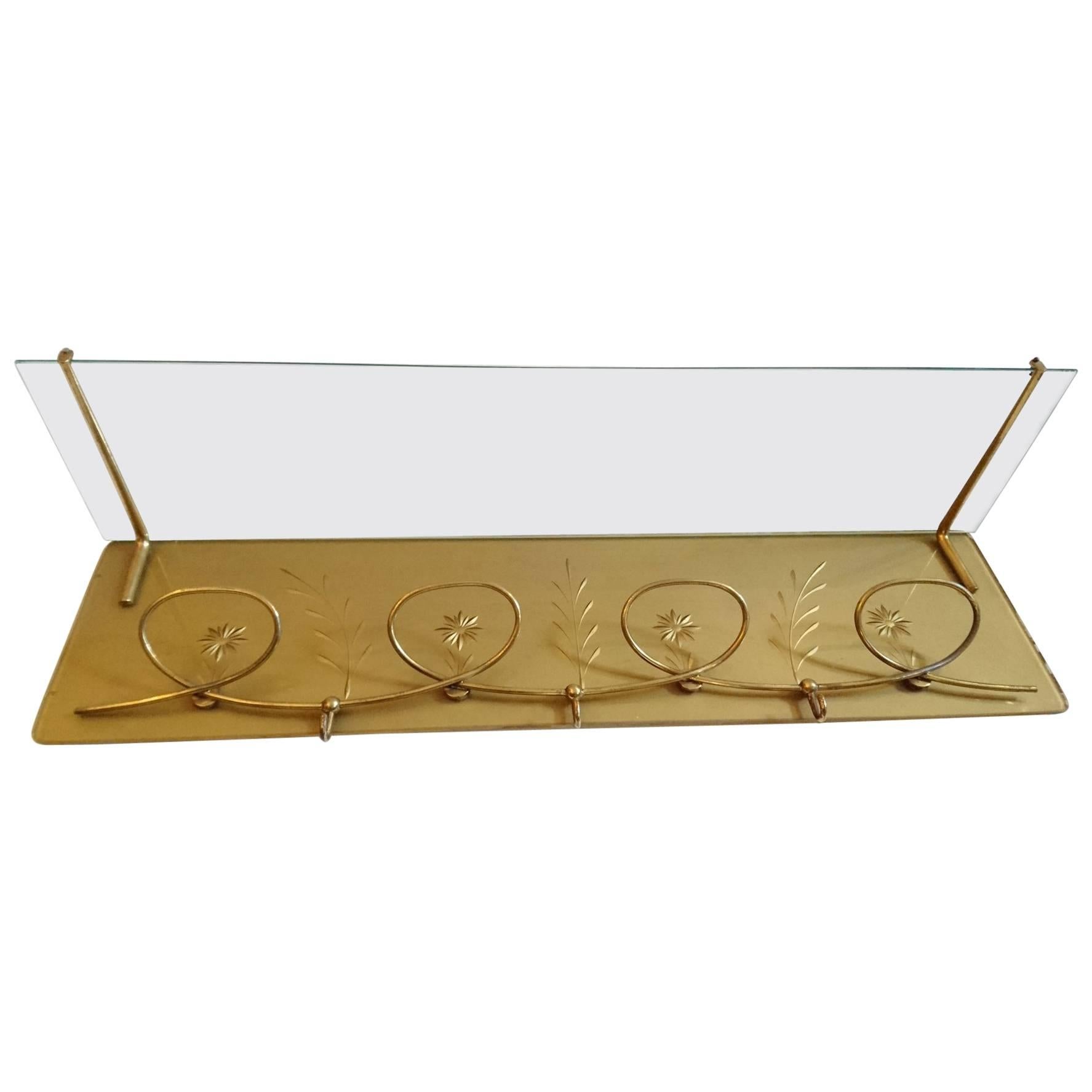 Elegant wall-mounted coat rack with a playful design in glass and brass and decorated with engraved flowers on gold base.