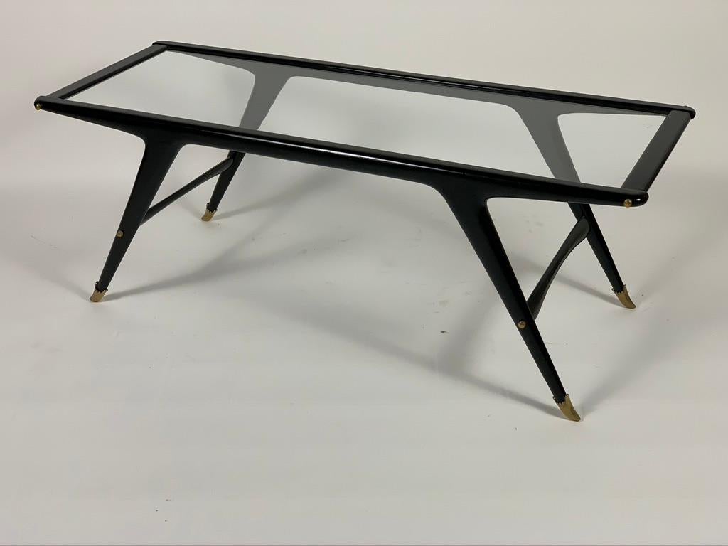 Low coffee table for living room with thin structure in black lacquered solid wood, top in ground and recessed glass, feet in brass casting details.
Due to its proportion, being shallow, this 1950s Italian coffee table is suitable for use in front