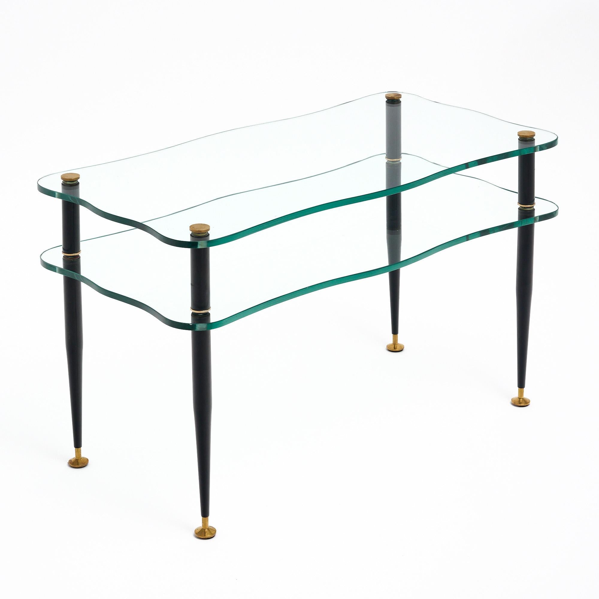 Coffee table from Italy in the mid-century style. This piece has four supportive brass legs lacquered in black. The legs hold two shelves of scalloped glass. We were drawn to the aesthetic elegance of this piece and the functional detail of the two