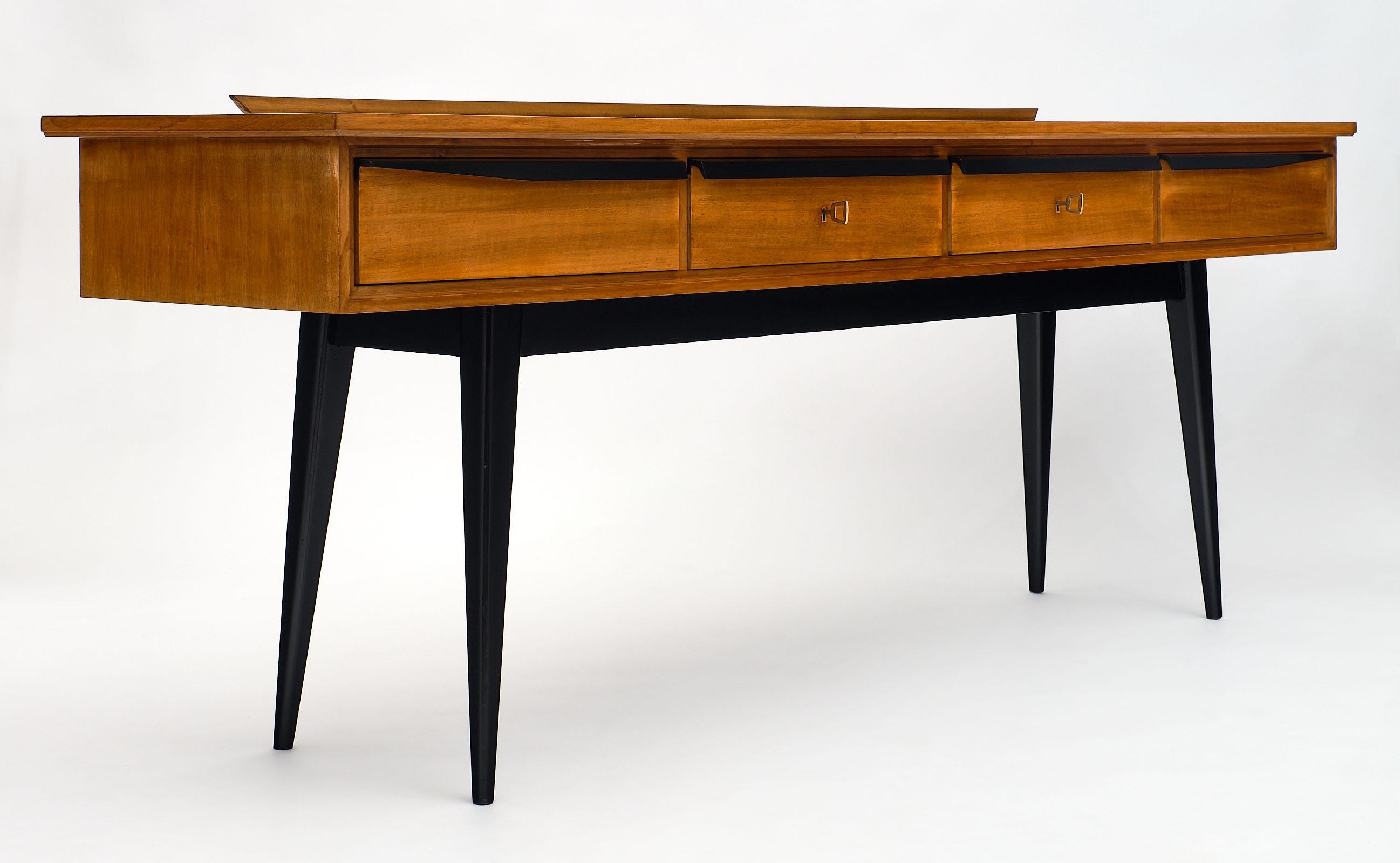 Italian midcentury console table with leather top made of sycamore. We love the tapered, flared legs which have been ebonized. The wooden handles are also ebonized on the four drawers. The center two drawers have original locks and keys in working