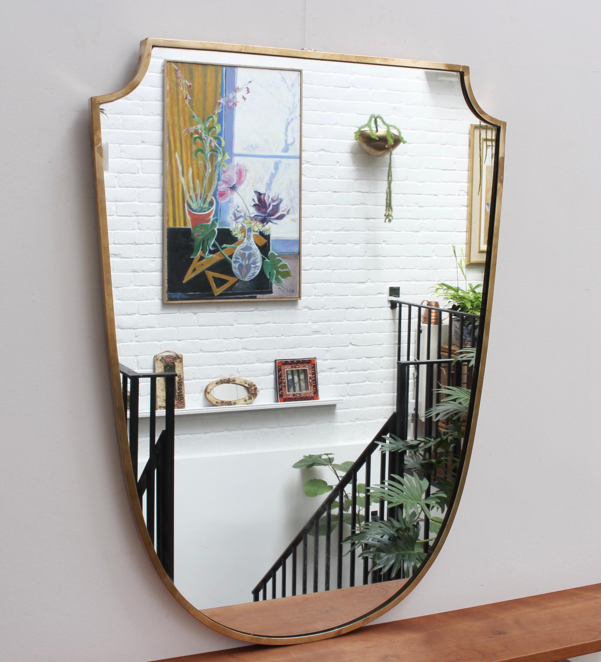Large vintage Italian wall mirror with brass frame (circa 1950s). The mirror is large with sensuous curves, solidity, weightiness and elegant good looks. The crest-shape is also powerful and imposing. It is in overall good vintage condition