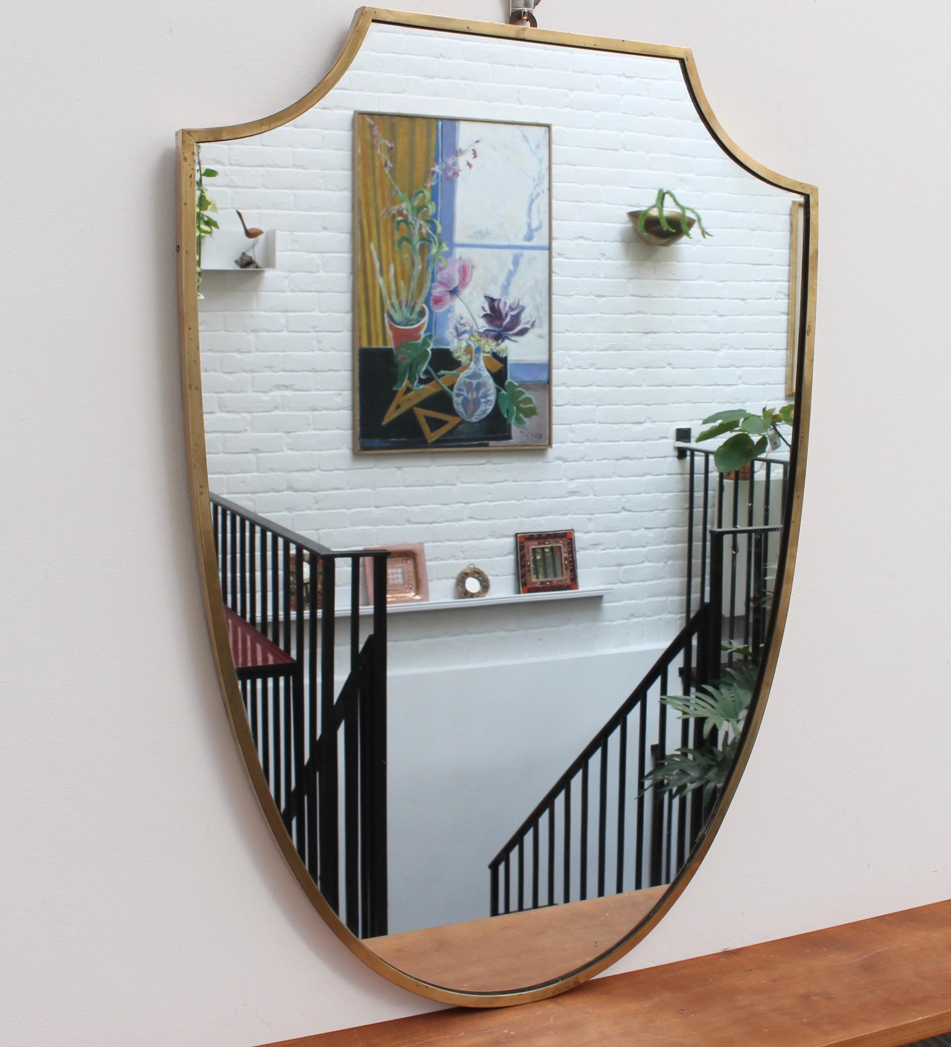 Midcentury Italian wall mirror with brass frame (circa 1950s). The mirror is substantial, crest-shaped - classically elegant in a modern Gio Ponti style. The piece is in overall good vintage condition with aged patina and some characterful