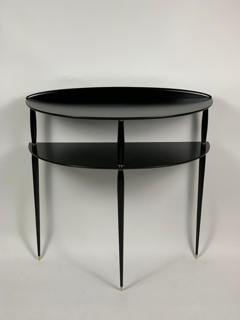 Four thin turned legs ending in a point with brass feet support two half moon shaped shelves, brass details finish the construction of this 1950s Italian console. Due to its slender structure, this midcentury console needs to be fixed to the wall by