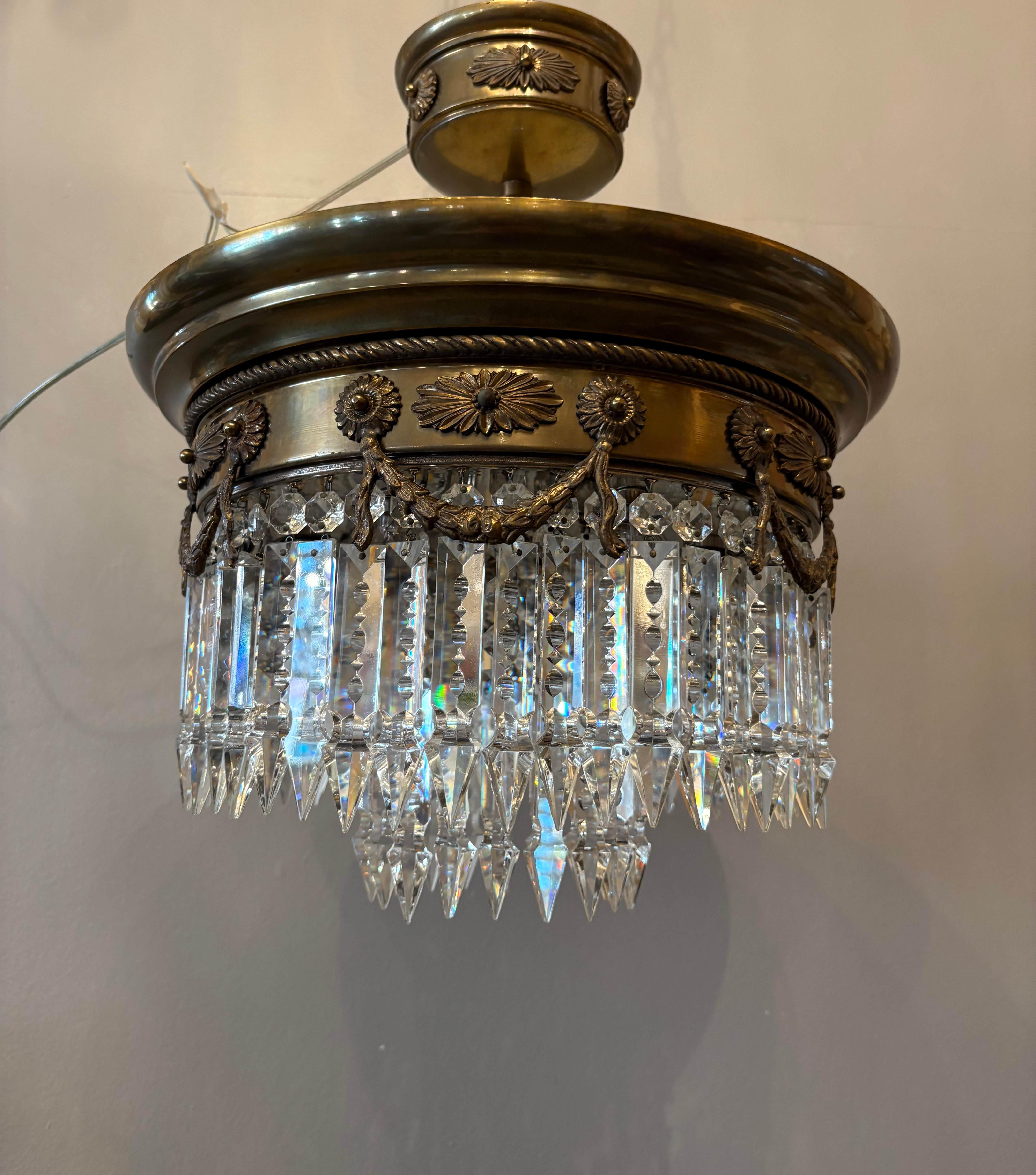 Elegante lámpara de araña de estilo Imperio italiano fabricada en la década de 1950, con un marco de latón chapado en bronce finamente detallado y adornado con motivos clásicos y guirnaldas drapeadas. La estructura circular se complementa