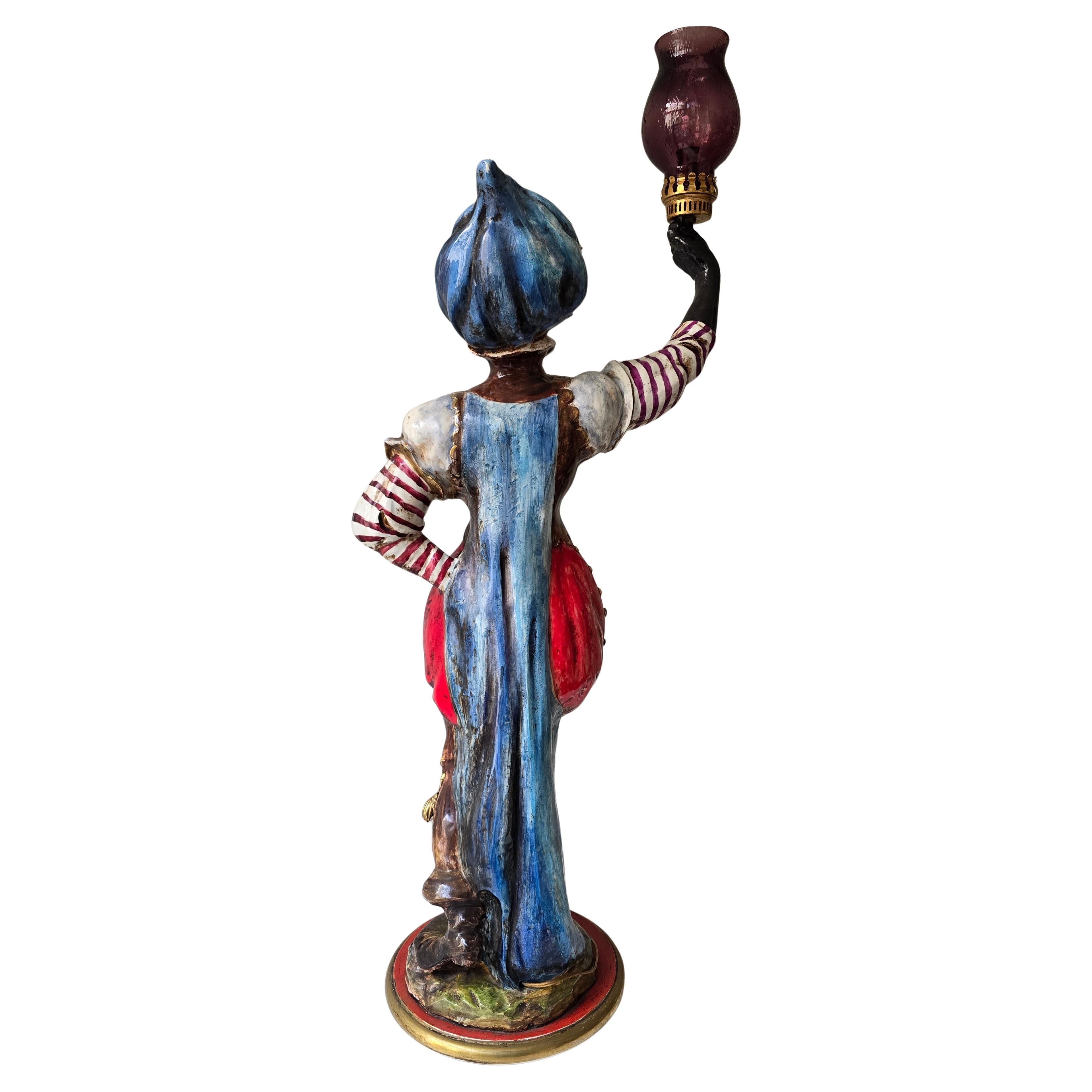 Elégante lampe figurative italienne du milieu du siècle, fabriquée à la main en céramique émaillée et peinte à la main, représentant un gentleman africain vêtu d'un costume richement coloré et tenant une lampe en forme de torche couronnée d'un