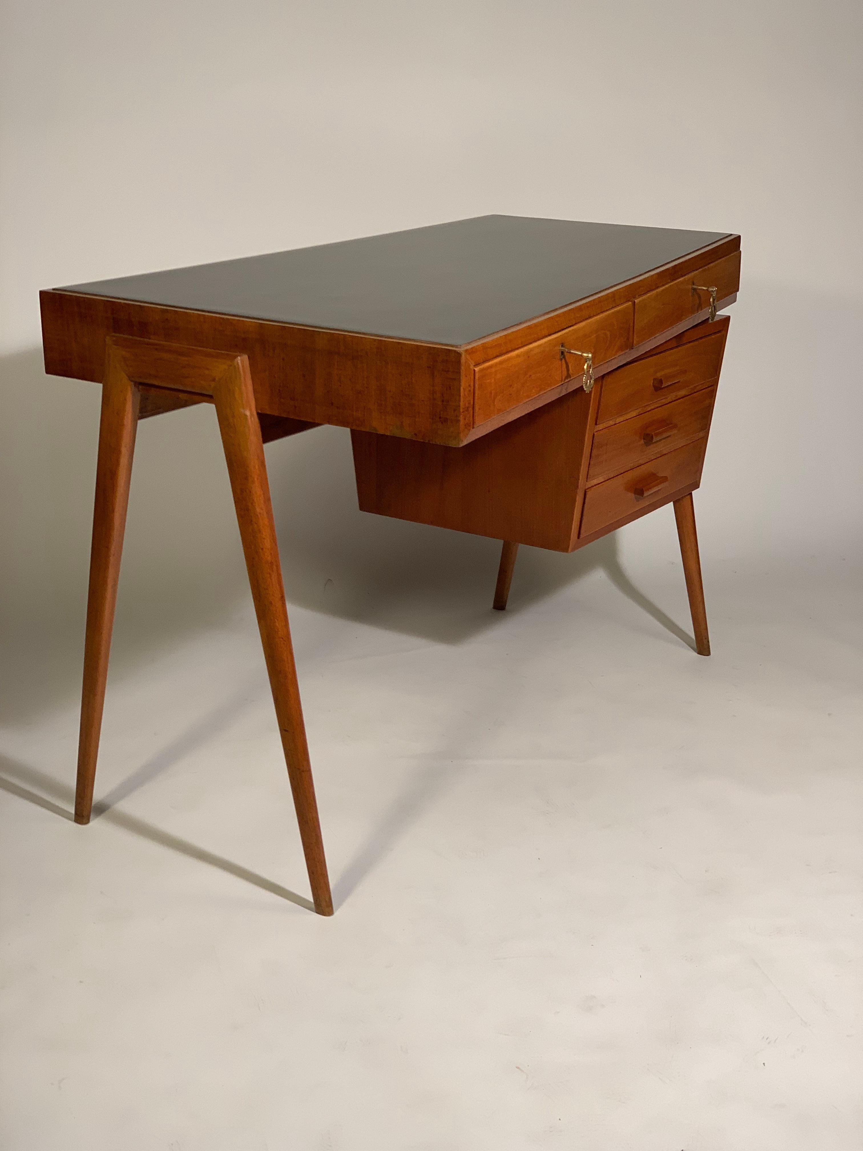 Writing desk with five drawers, two larger ones arranged under the top and three drawers on a chest of drawers arranged oblique respect to the top ,with three sculptured handles . Trapezoid-shaped black formica top with a smaller side under which