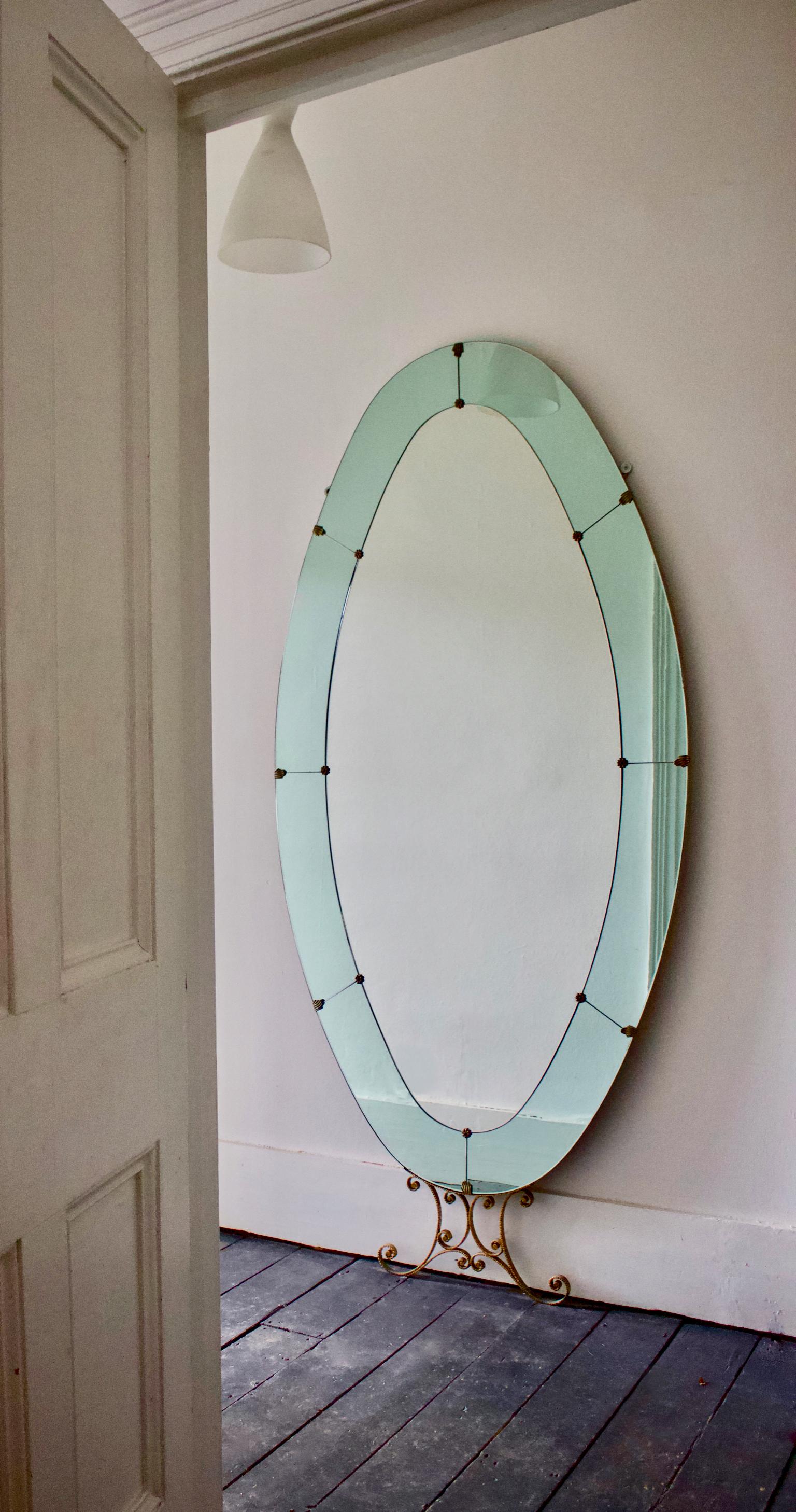 Mid-20th century Italian floor-standing oval mirror with blue border and decorative metal stand, attributed to Pier Luigi Colli. 

The clear central mirror is surrounded by a border in eight sections of delicate mirror glass tinted a beautiful shade