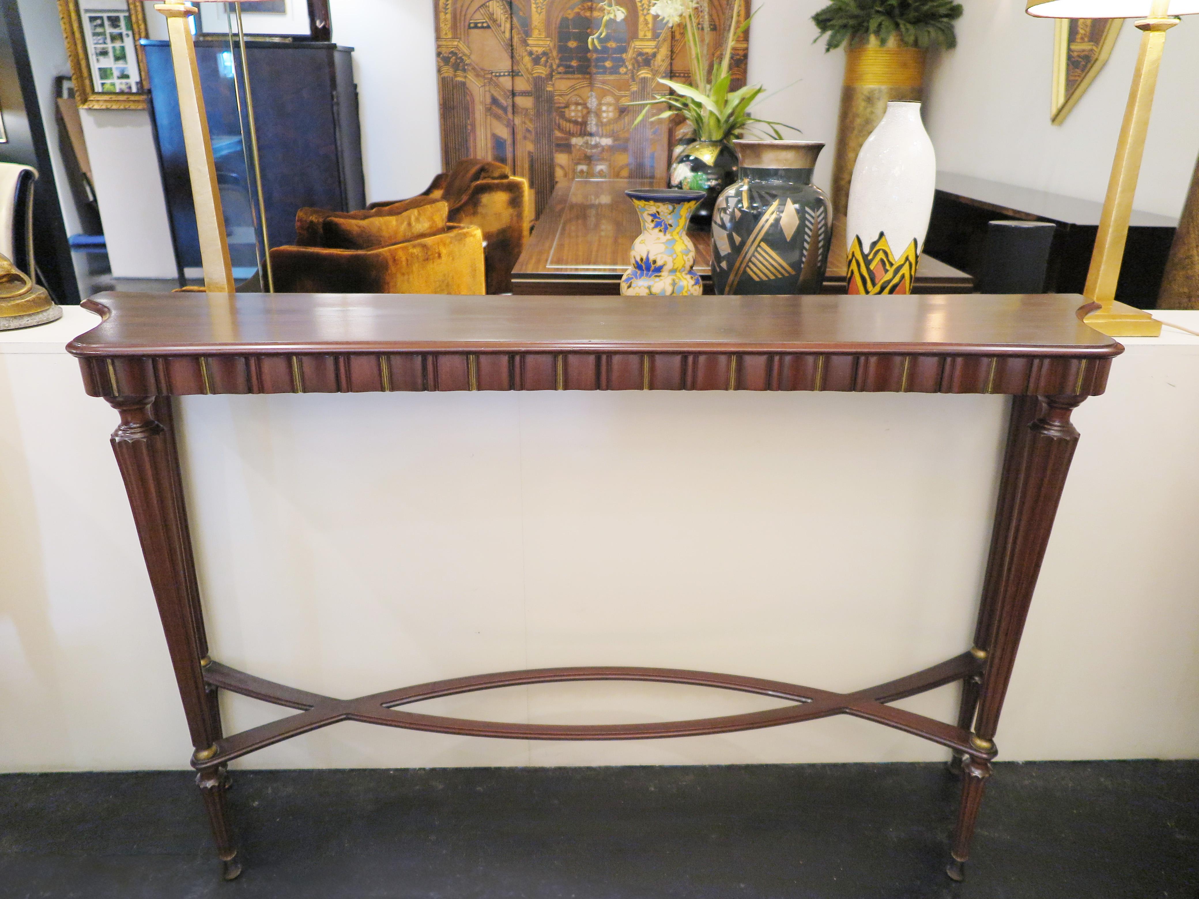 Italian Mid-Century console in mahogany with beautiful fluted detailing along facade and sides. Four ribbed tapered legs support the delicate frame. The original brass hardware and leaf accents add the finishing touch. The back plate along the top