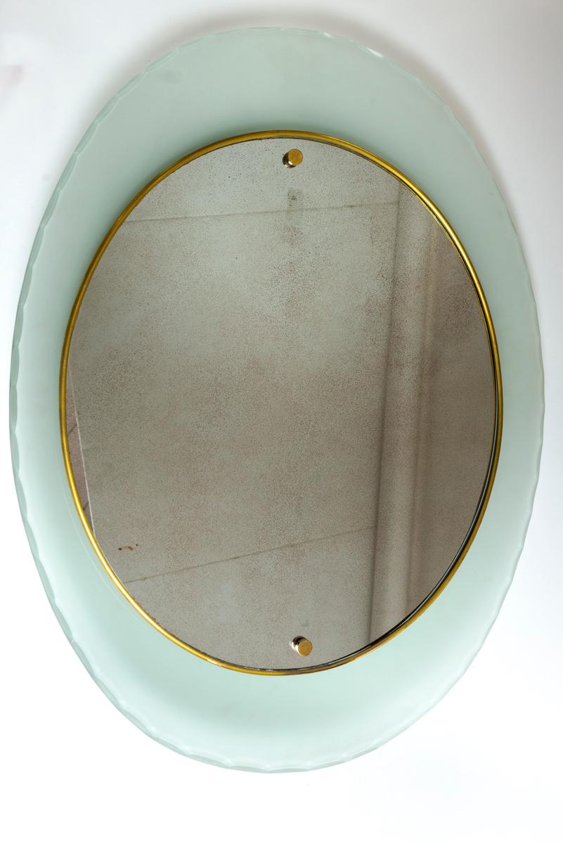 An elegant and unique curved frosted and scalloped cut glass frame holding a near circular brass framed looking glass.  The looking glass is beautifully antiqued offering a gentle reflection.  The curved frame is frosted on its back side and the