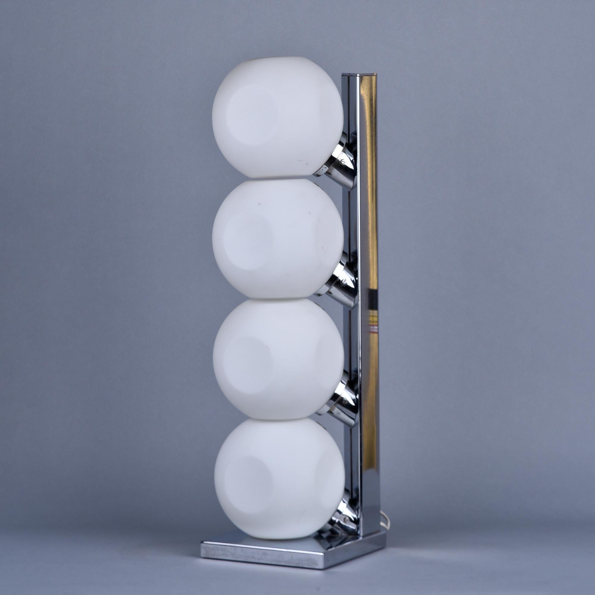 Found in Italy, this circa late 1960s / early 1970s table tamp features four white glass globes stacked at an angle on a polished metal base. Glass globes have disc shaped panels and each covers a candelabra sized socket. Unknown maker. 

Lamp has