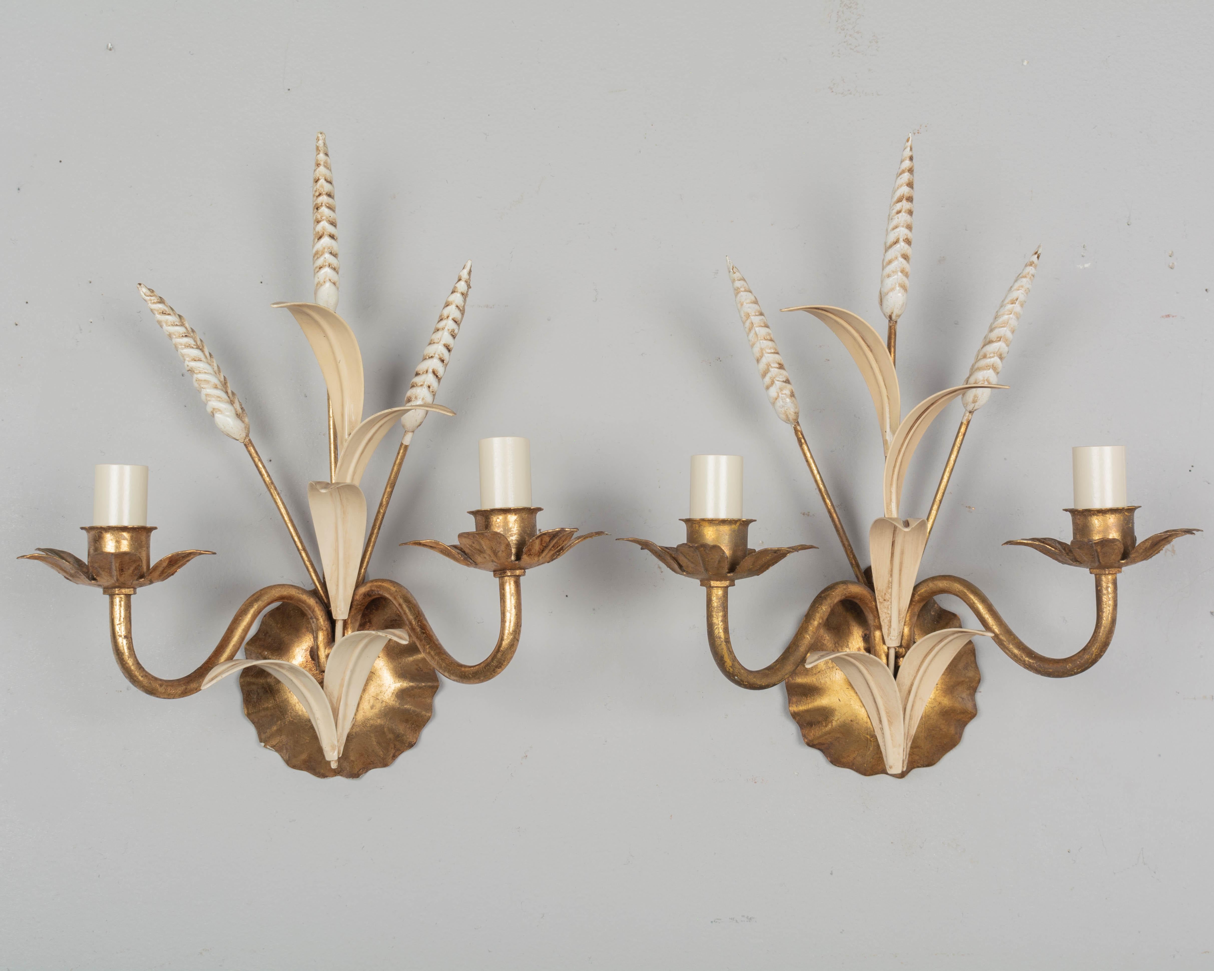 A pair of Hollywood Regency style two-light gilt metal sconces with painted tôle leaves and wheat stems. Designed by Hans Kögl and made in Italy. New sockets and candle covers. Wired and in working order. Circa 1960-1970. 
Dimensions: 10.5