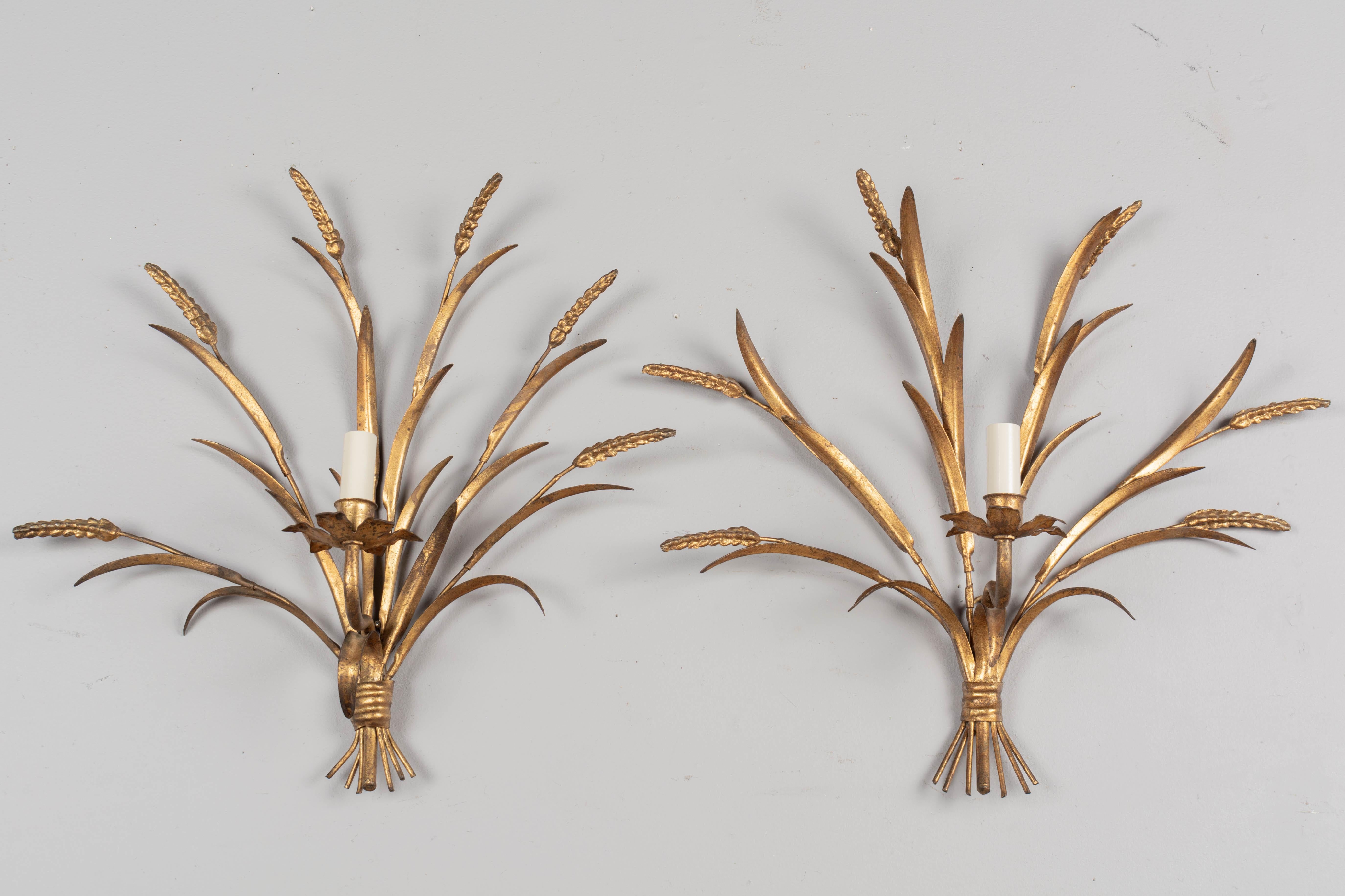 A pair of Hollywood Regency style gilt metal sconces with tôle leaves and wheat stems. Designed by Hans Kögl and made in Italy. New sockets and candle covers. Wired and in working order. Circa 1960-1970. 
Dimensions: 19