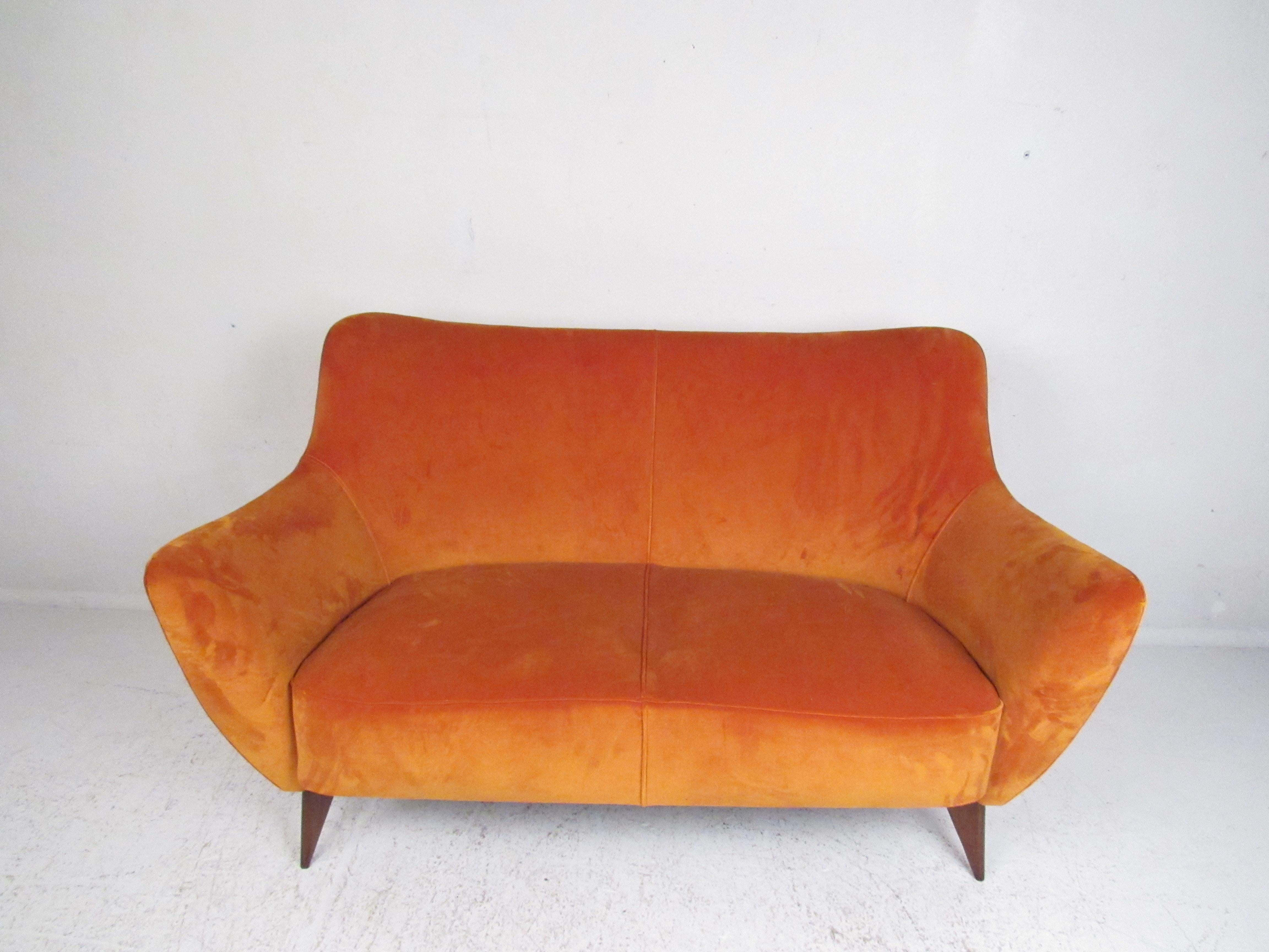 This elegant vintage modern sofa features splayed walnut legs, winged armrests, and a thick padded seat. The elegant orange velour upholstery makes this piece pop in any seating arrangement. In the style of Gio Ponti. Please confirm item location
