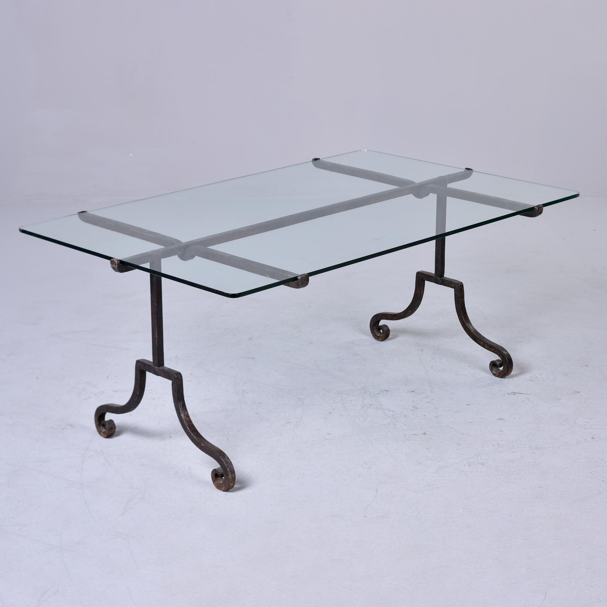 Found in Italy, this cocktail or coffee table dates from the 1970s and has an iron base and thick glass top. The dark wrought iron base has pleasing simple lines with scrolled feet and a 1/2” thick glass top that is securely held by fitted grooves