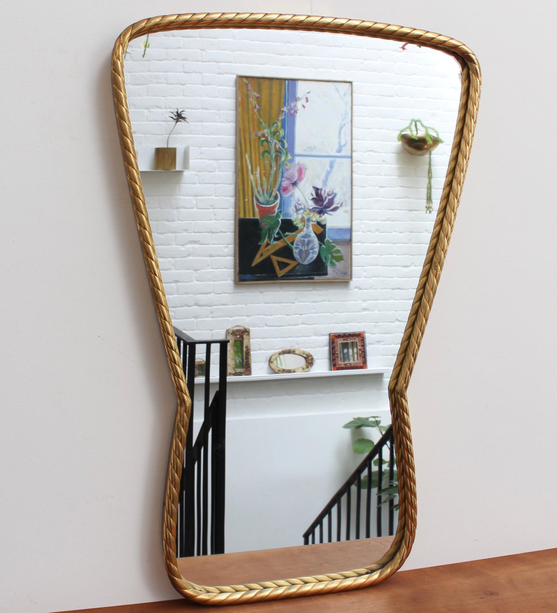 Vintage Italian wall mirror in brass frame with stranded rope pattern, (circa 1950s). The mirror has presence with distinctive lines and elegant good looks. The keyhole-shape with stranded rope pattern is unique and rarely found on the vintage