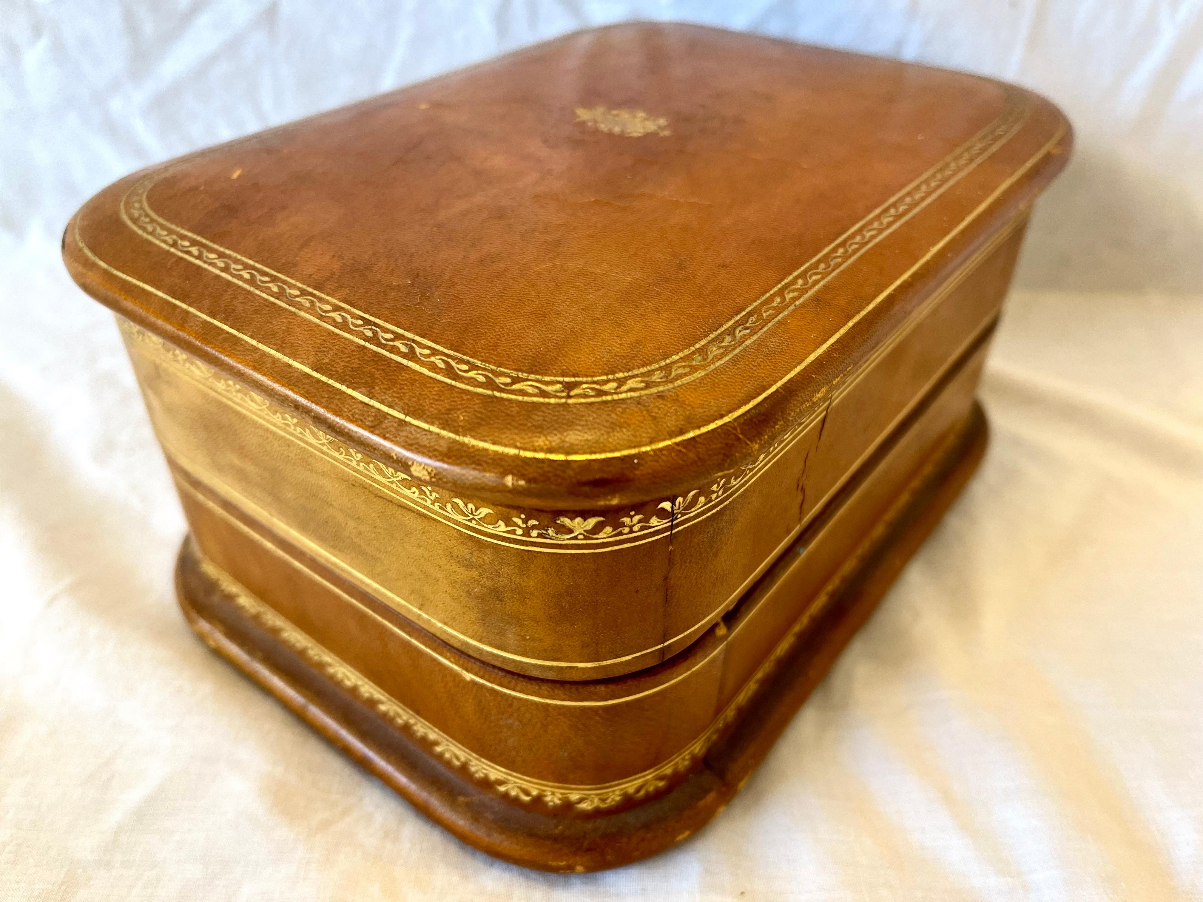 A gorgeous mid century Italian stencil gilt leather hinged top jewelry casket or box with suede lined interiors, swing out tray and two fitted pillows. This Italian box was ‘made expressly for Saks Fifth Avenue’ in New York City. The patina on the