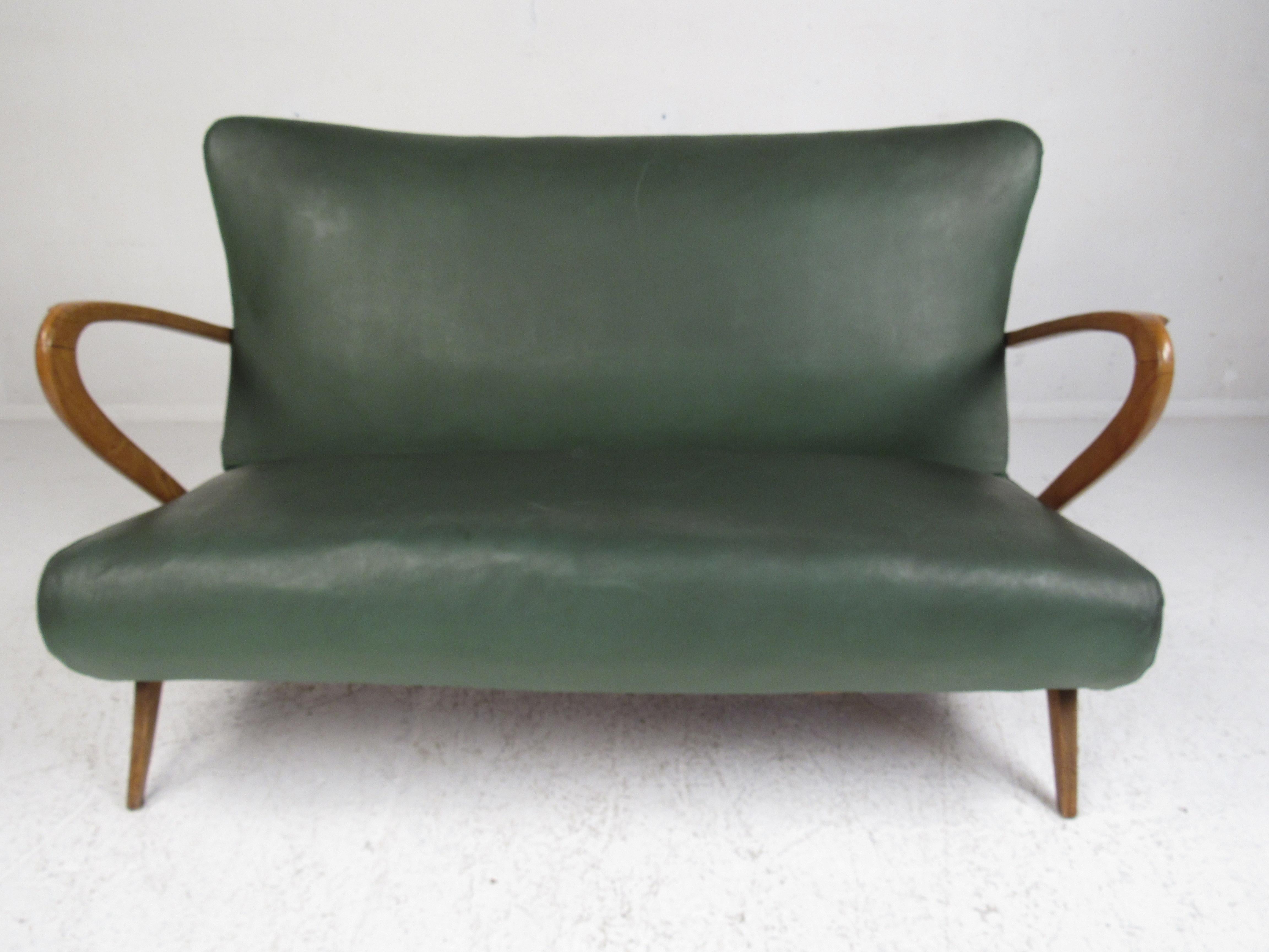 This stunning vintage modern sofa boasts a sculpted oak frame with curved armrests and angled legs. A sleek and comfortable design covered in green vinyl. This wonderful Paolo Buffa style settee is sure to fit any seating arrangement. Please confirm