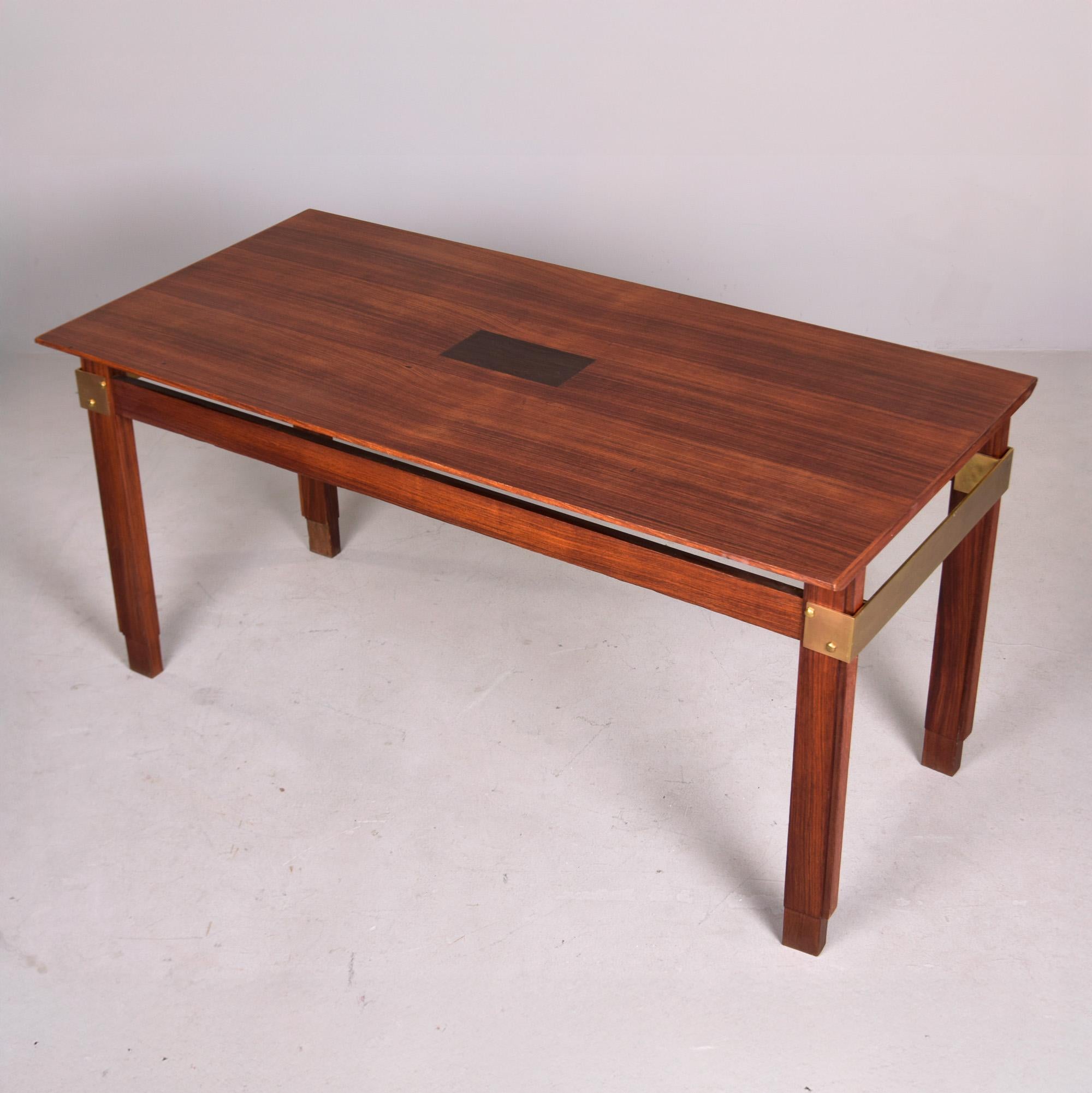 Trouvée en Italie, cette table de salle à manger en acajou et laiton date des années 1970. La table présente un plateau joliment figuré avec un accent central contrasté, des pieds rectangulaires, des supports en laiton enveloppants aux extrémités et