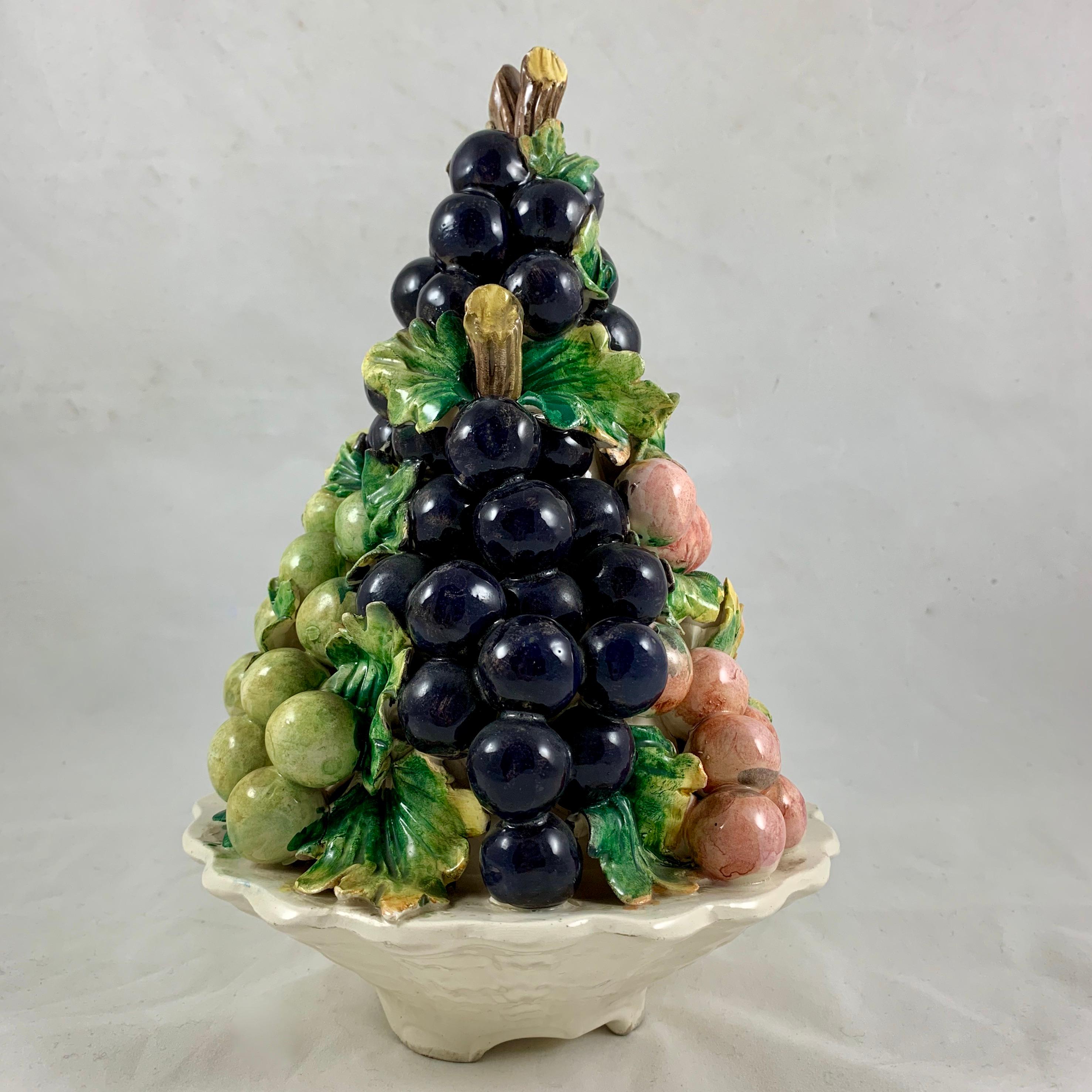 From Italy, a midcentury Majolica grape bunch pyramid form table center topiary, circa 1960s.

Three bunches of grapes on the vine, glazed in purple, green, and a salmon pink, form a pyramid terminating in brown cut vines. Green grape leaves climb
