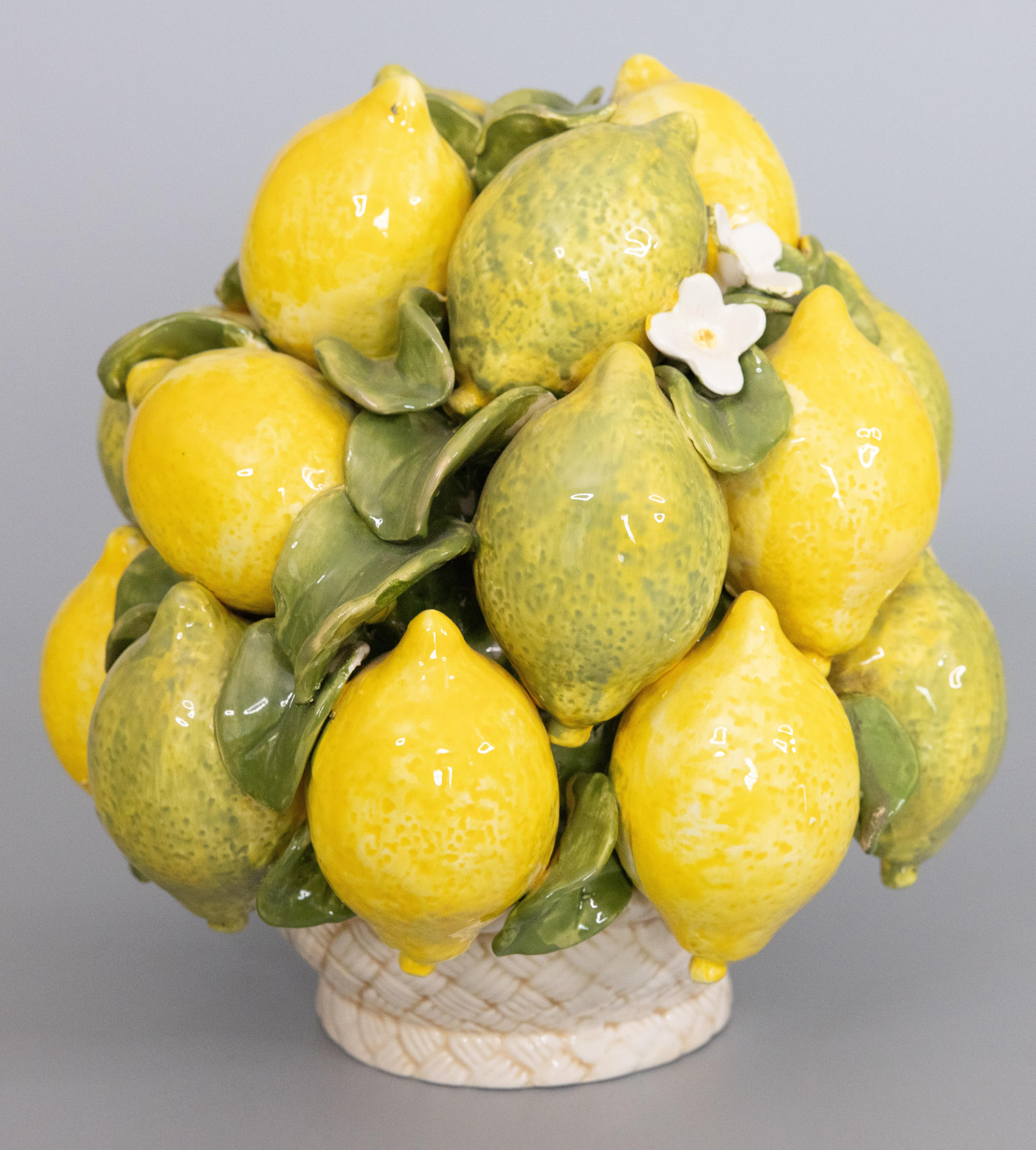 A lovely Mid Century Italian majolica lemons and limes topiary basket table centerpiece. Brighten up your kitchen or dining room with this beautiful hand painted arrangement of lemons and limes, accented by vibrant green leaves and flowers, in a