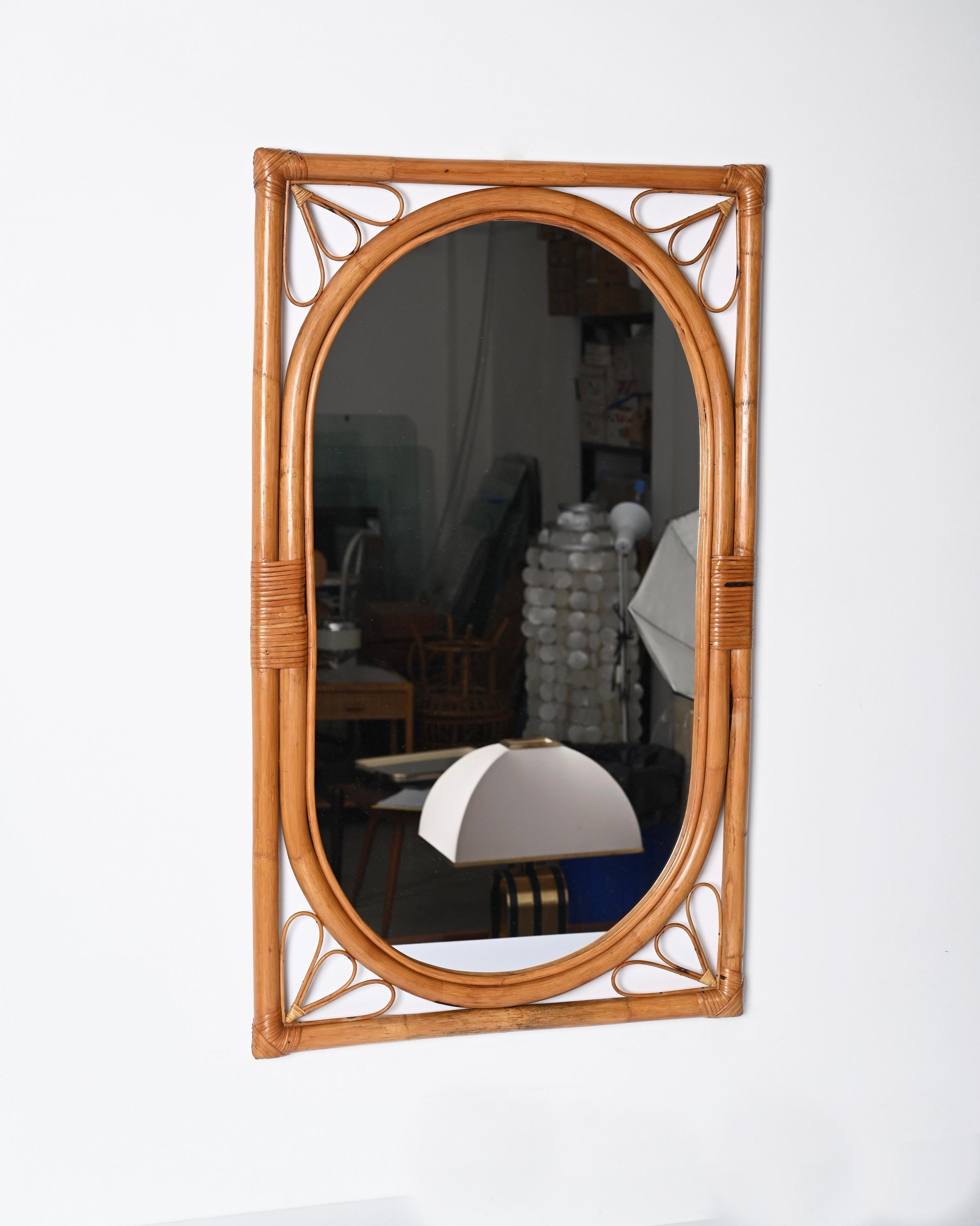 Marvellous midcentury mirror with double bamboo frame and rattan decorations. This fantastic item was produced in Italy in the 1970s.

This gorgeous mirror features an external rectangular bamboo frame and an internal oval frame that holds the
