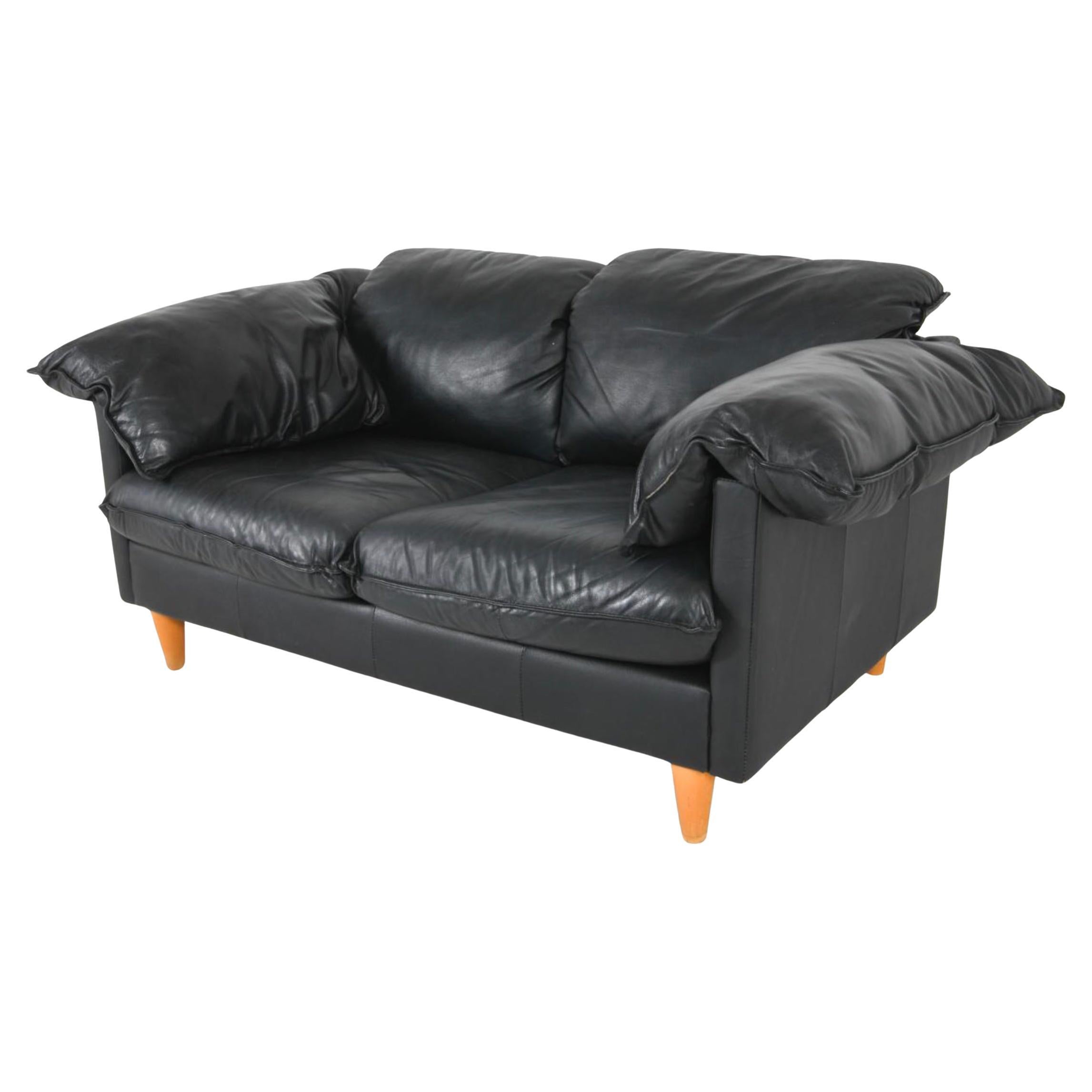 Divano moderno di metà secolo in pelle nera. Divano a 2 posti dal design e dalla forma confortevoli, con cuscini per i braccioli che poggiano su 4 grandi gambe tonde e affusolate in legno di betulla. Ottime condizioni vintage, pronto per l'uso.