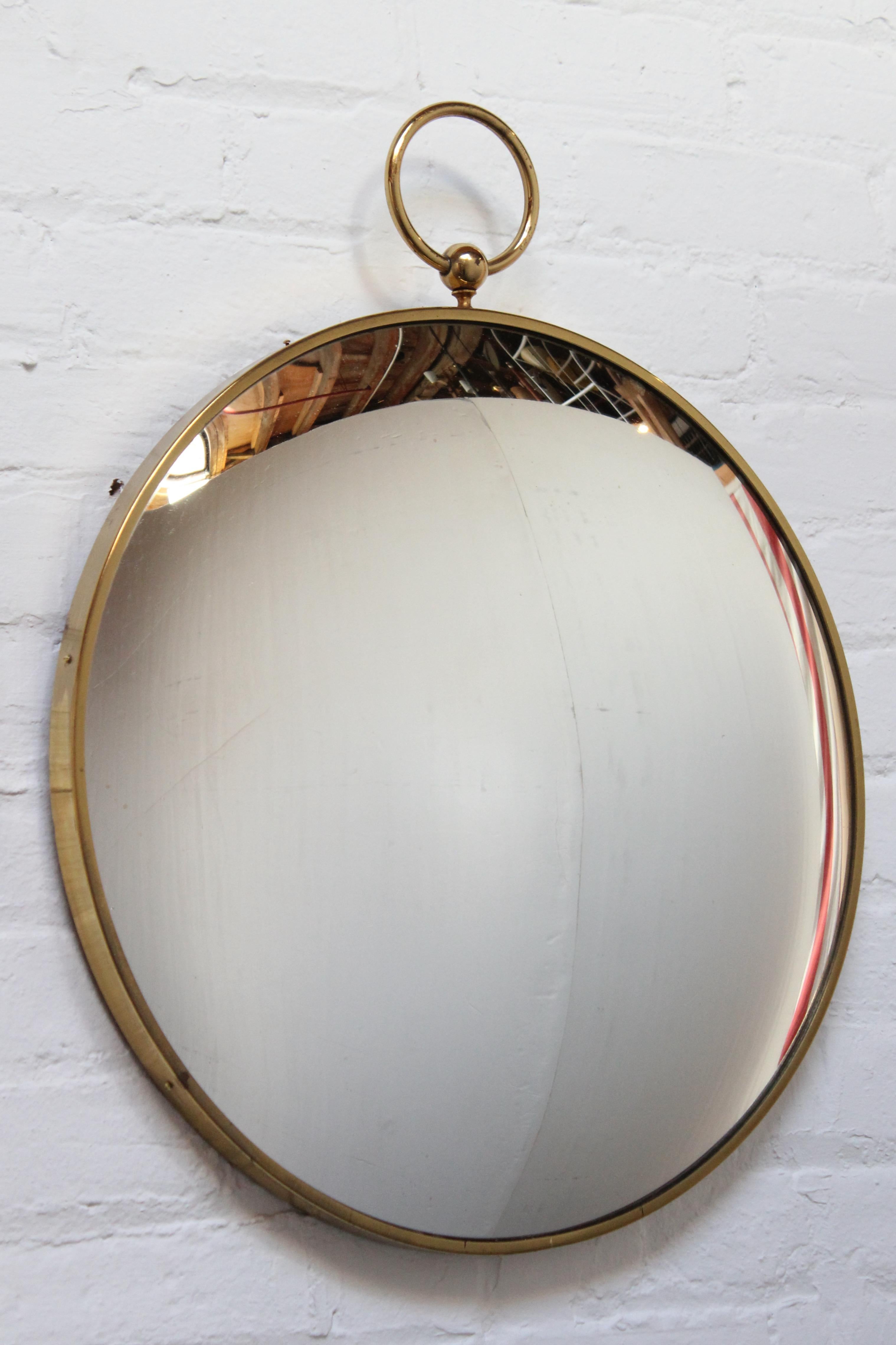 Pocket-watch form mirror in the style of Piero Fornasetti (ca. 1950s, Italy) composed of inset convex glass housed in a brass frame with a walnut backing. 
Patina / light tarnish / discoloration to the unpolished brass. There are a couple very