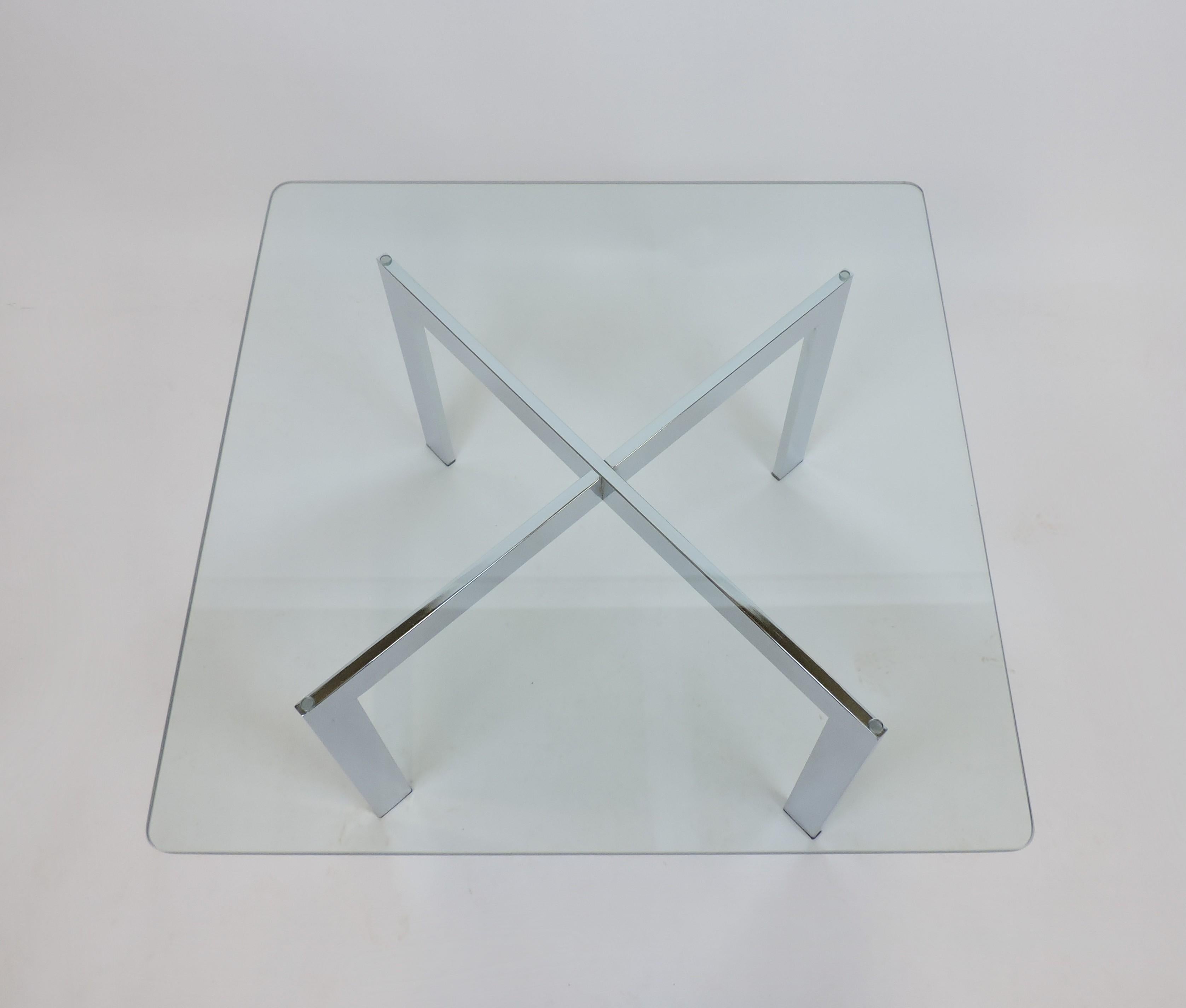 Table basse ou d'appoint classique de style barcelonais à base en X. Cette table est dotée d'une base chromée et d'un lourd plateau en verre transparent de 1/2