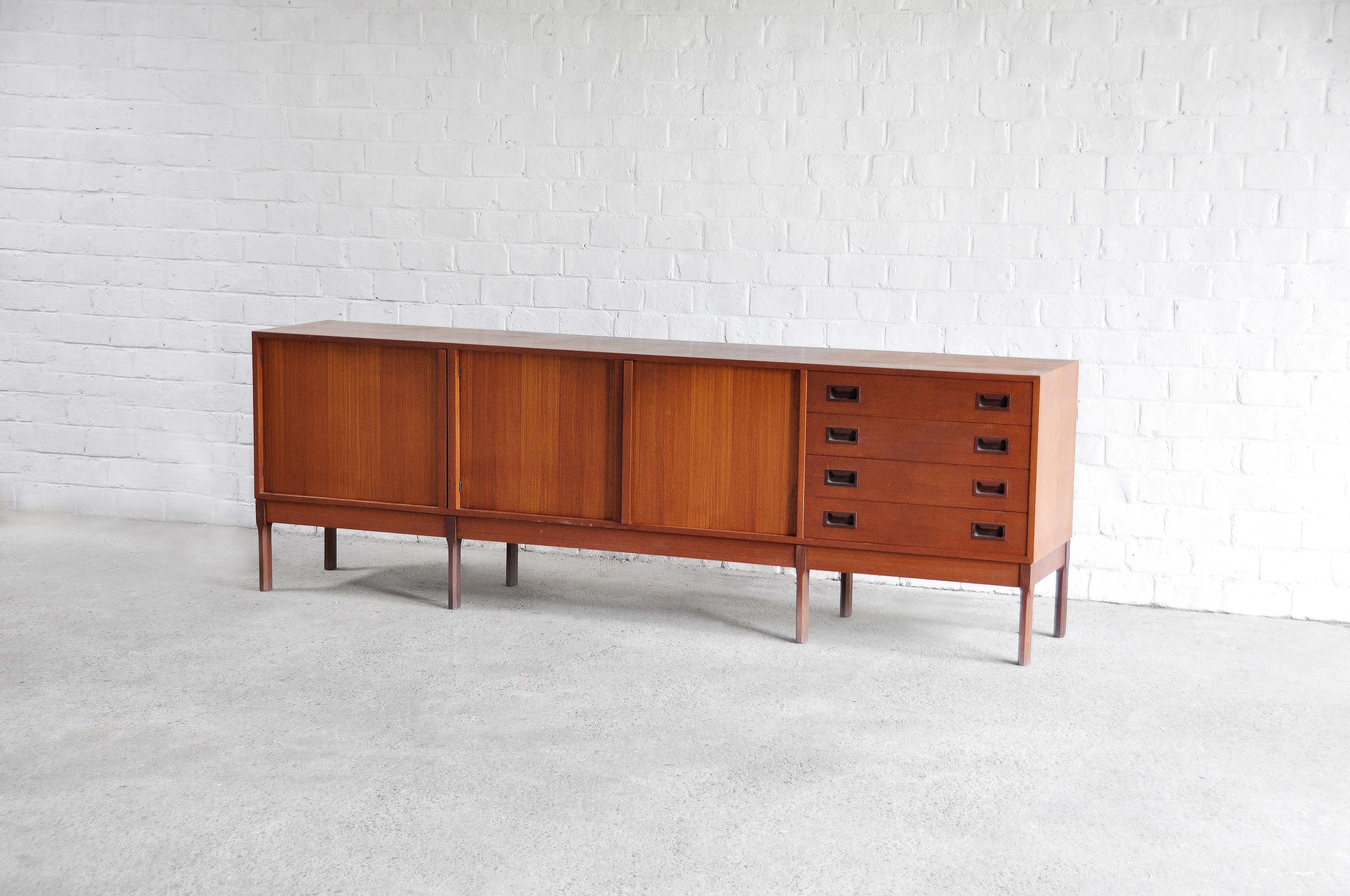 A beautiful Italian midcentury teak sideboard with four drawers and three sliding doors. The colored teak wood brings a warm feel to the design. The cabinet stands on a wooden structure of eight legs. Remains in good vintage condition, wear