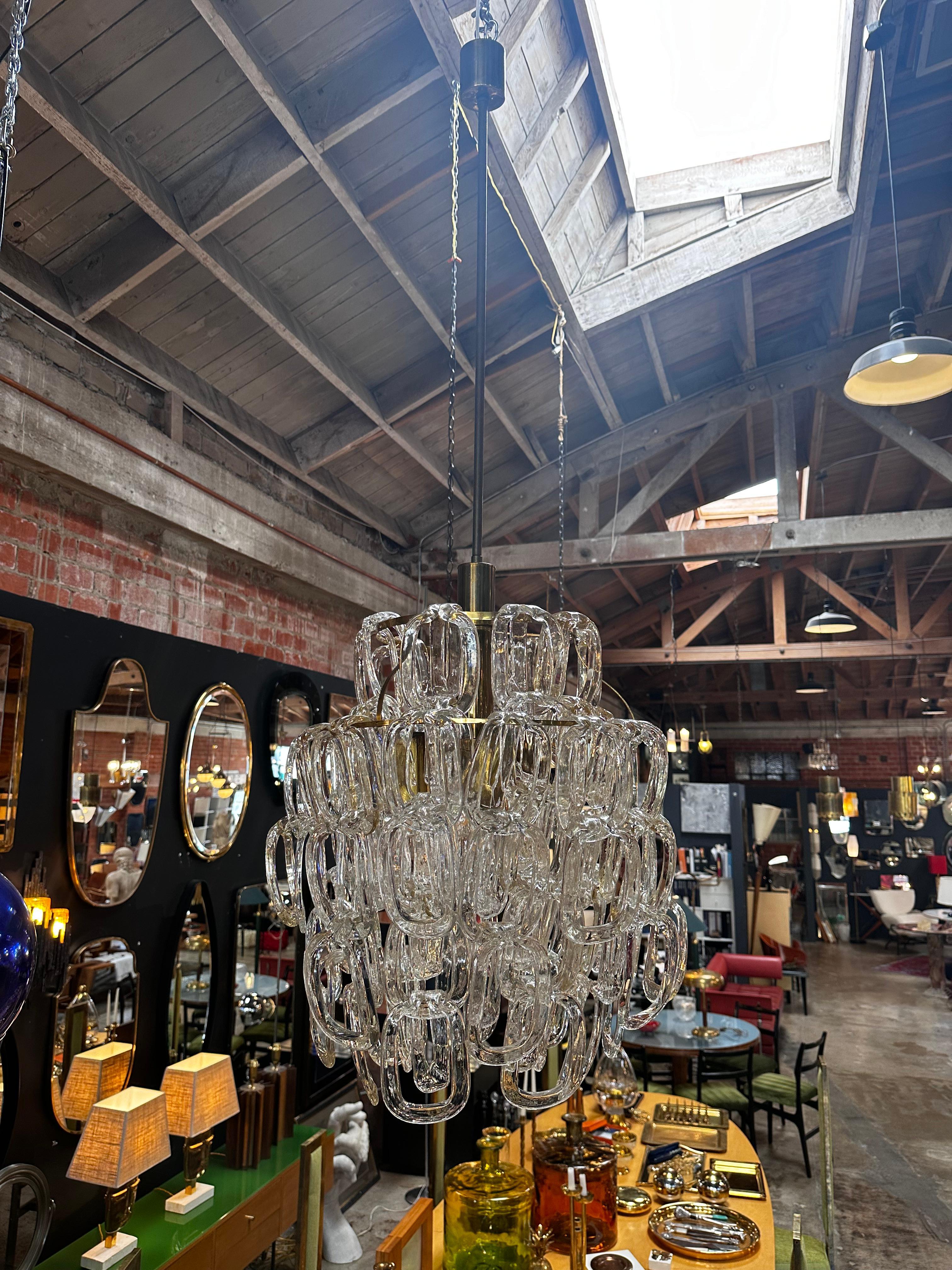 The Murano chandelier crafted in Italy in 1980 features a stunning design with a brass base and cascading Murano glass chain pieces, creating a captivating visual cascade of elegance and craftsmanship.
