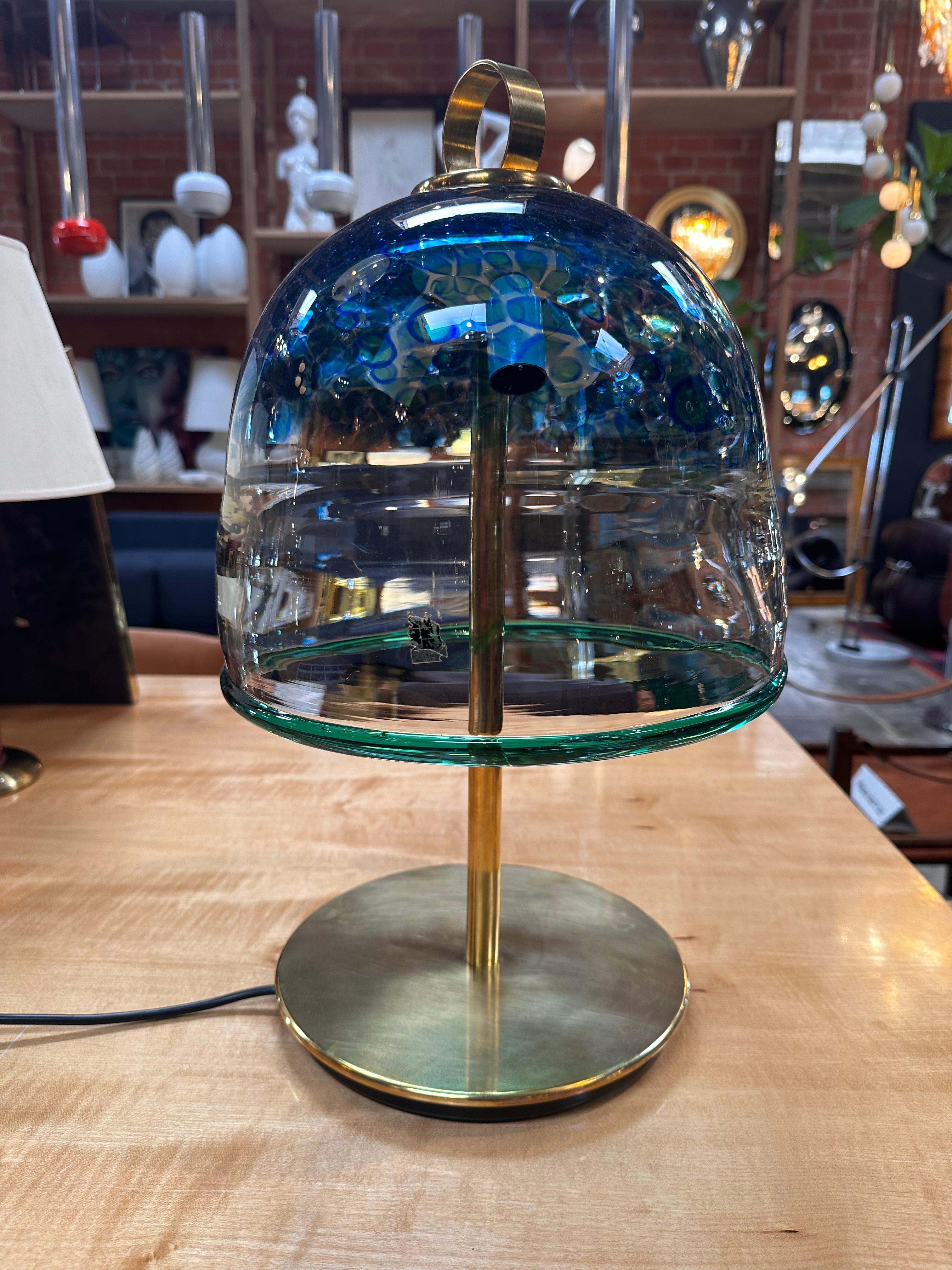 A Mid-Century Italian Murano Table Lamp from the 1960s features a distinctive design with a brass base and a uniquely styled fully blue Murano shade. This lamp encapsulates the elegance and innovation of mid-century Italian craftsmanship, making it